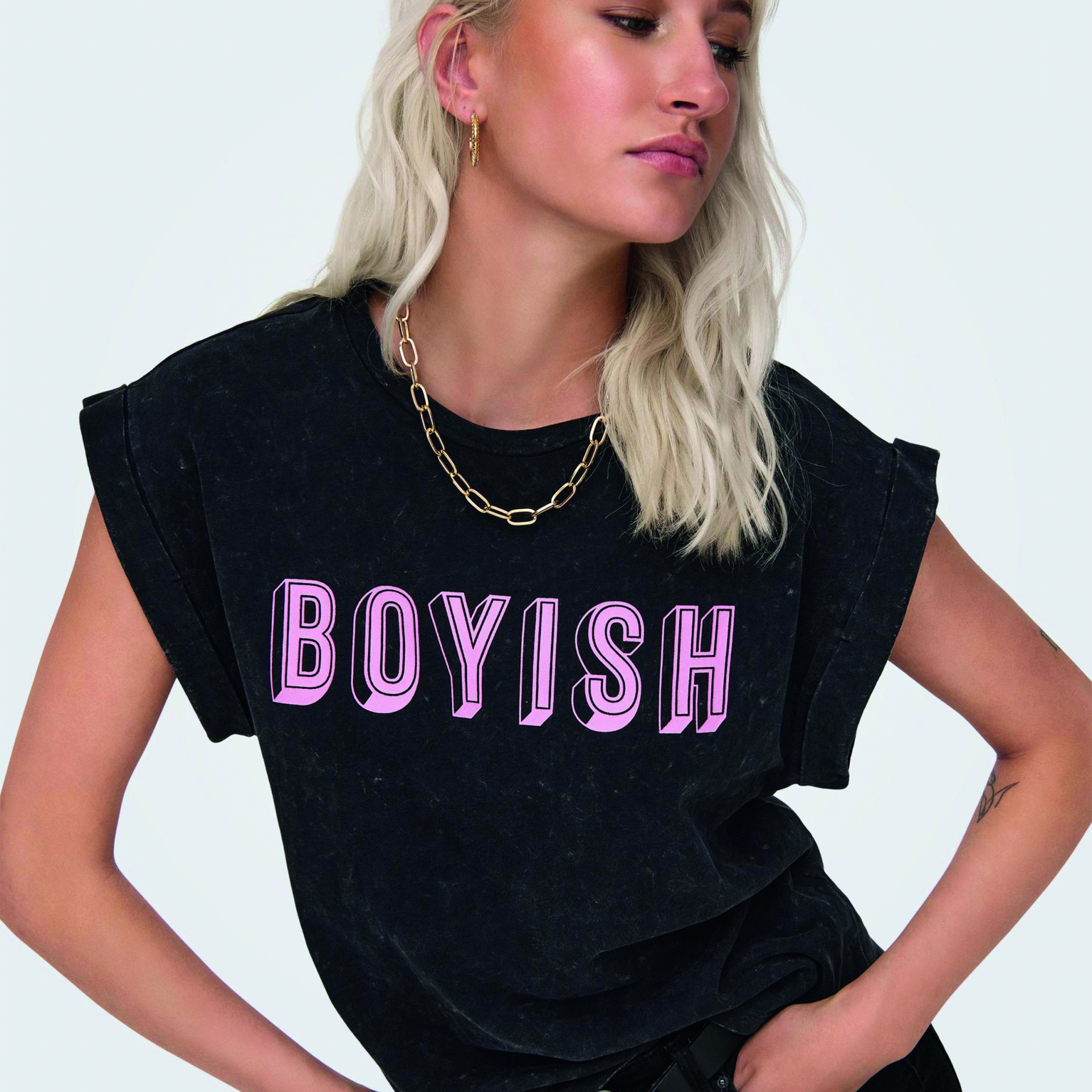 Mulher com t-shirt preta estampada BOYISH em letras cor-de-rosa