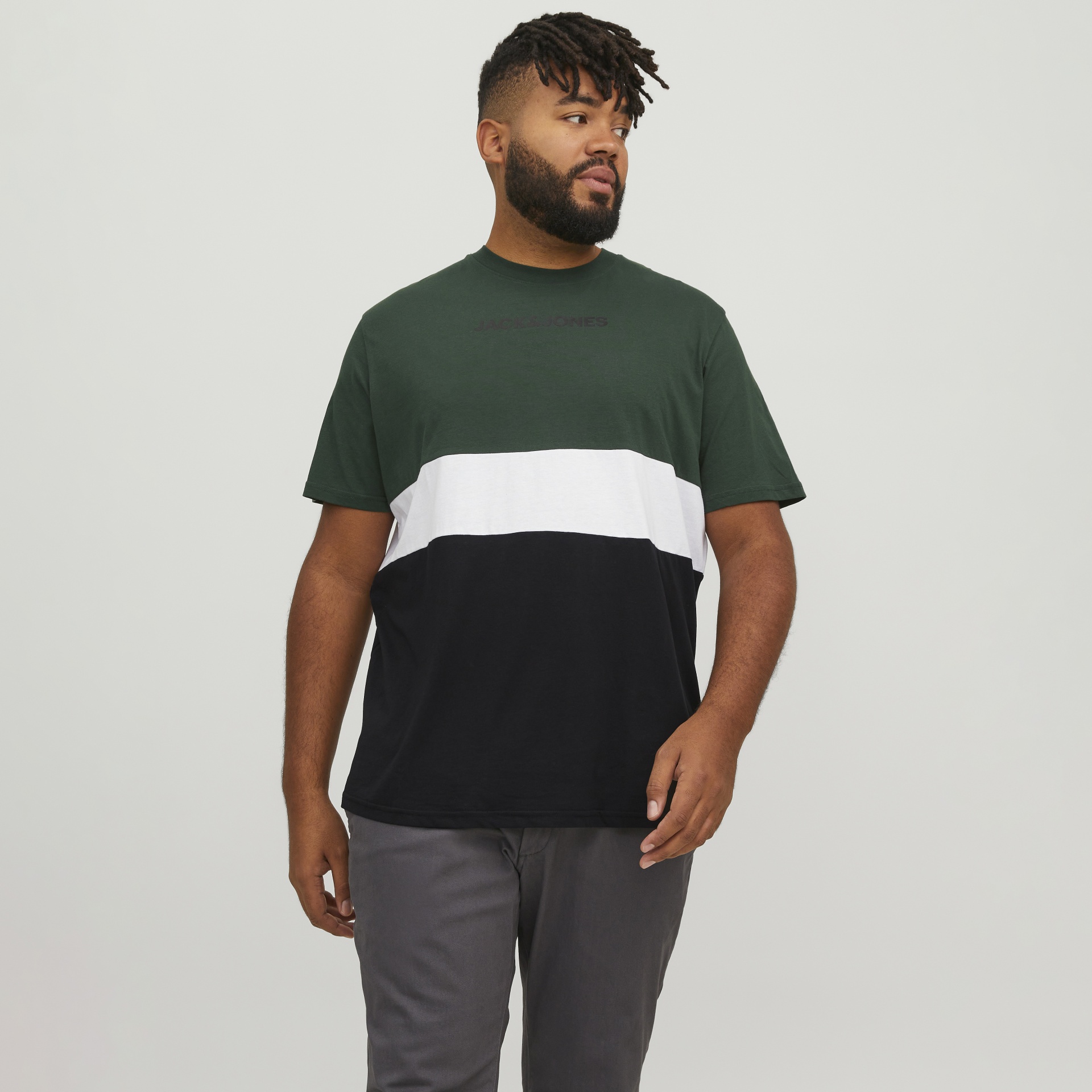 Homem com t-shirt verde, branca e preta com texto JACK & JONES e calças cinza em fundo branco