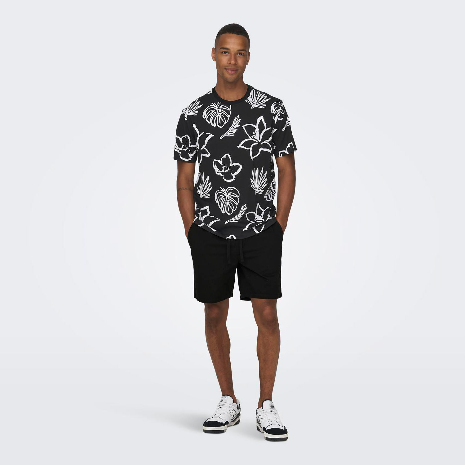 Homem com t-shirt preta estampada, calções pretos e sapatilhas brancas