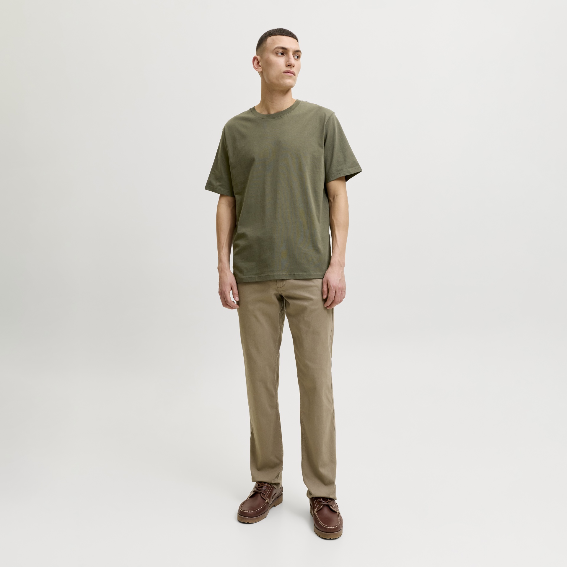 Homem com t-shirt verde-oliva, calças bege e sapatos castanhos em fundo branco