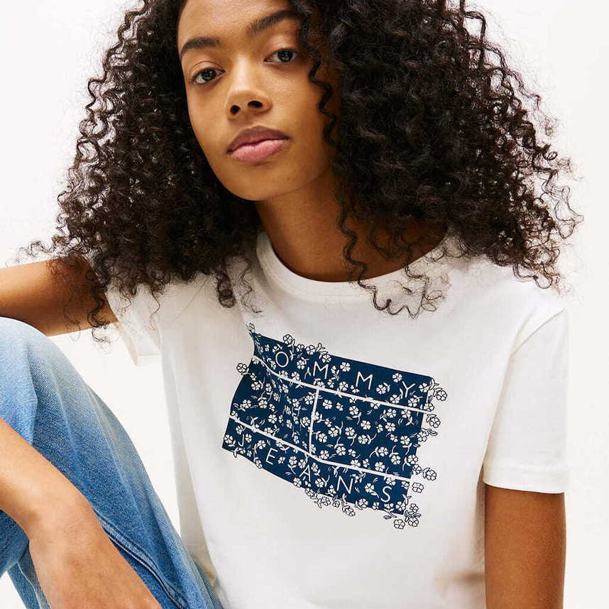 Mulher com t-shirt branca Tommy Jeans com estampa azul floral e calças de ganga