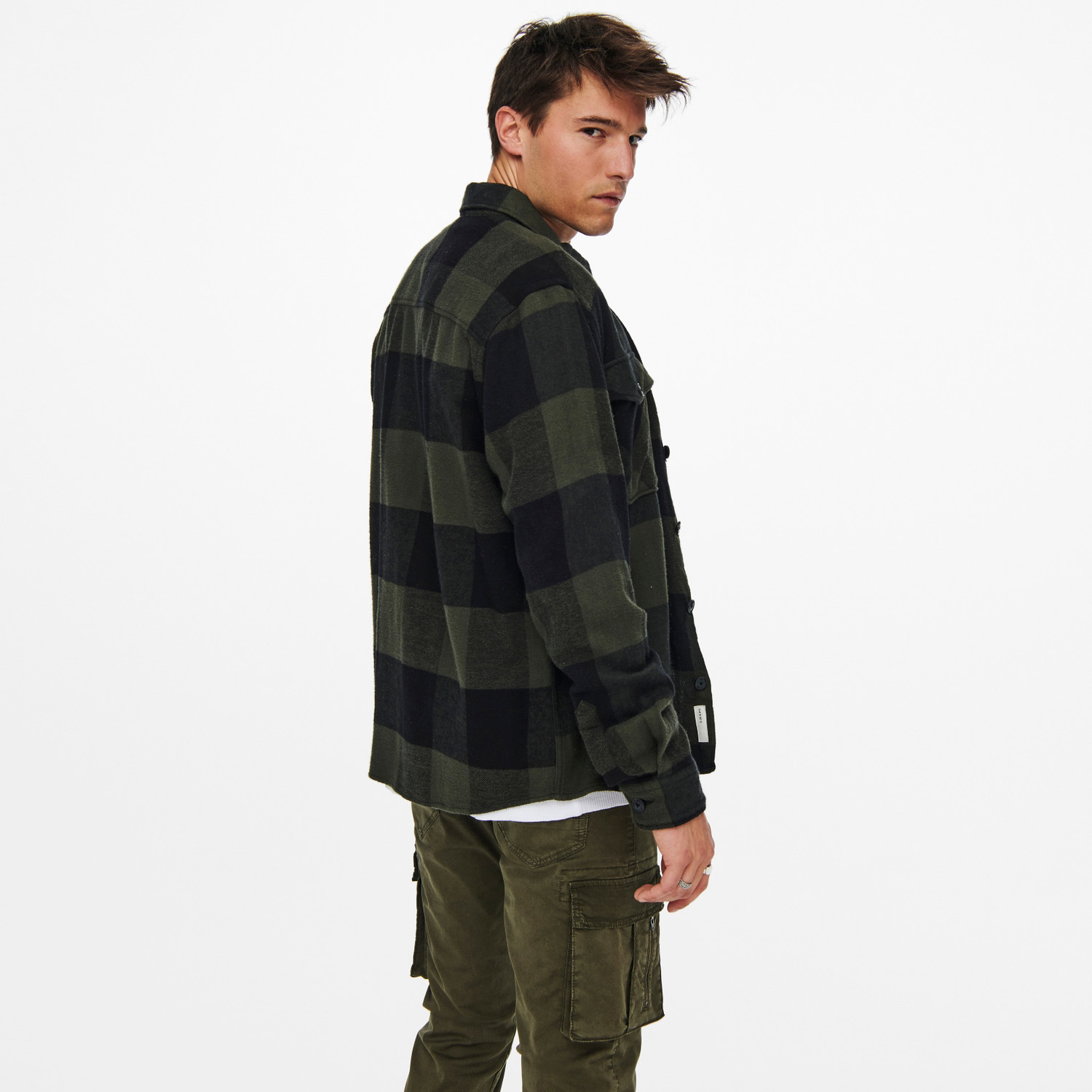 Homem com camisa xadrez verde e preta e calças cargo verdes em fundo branco
