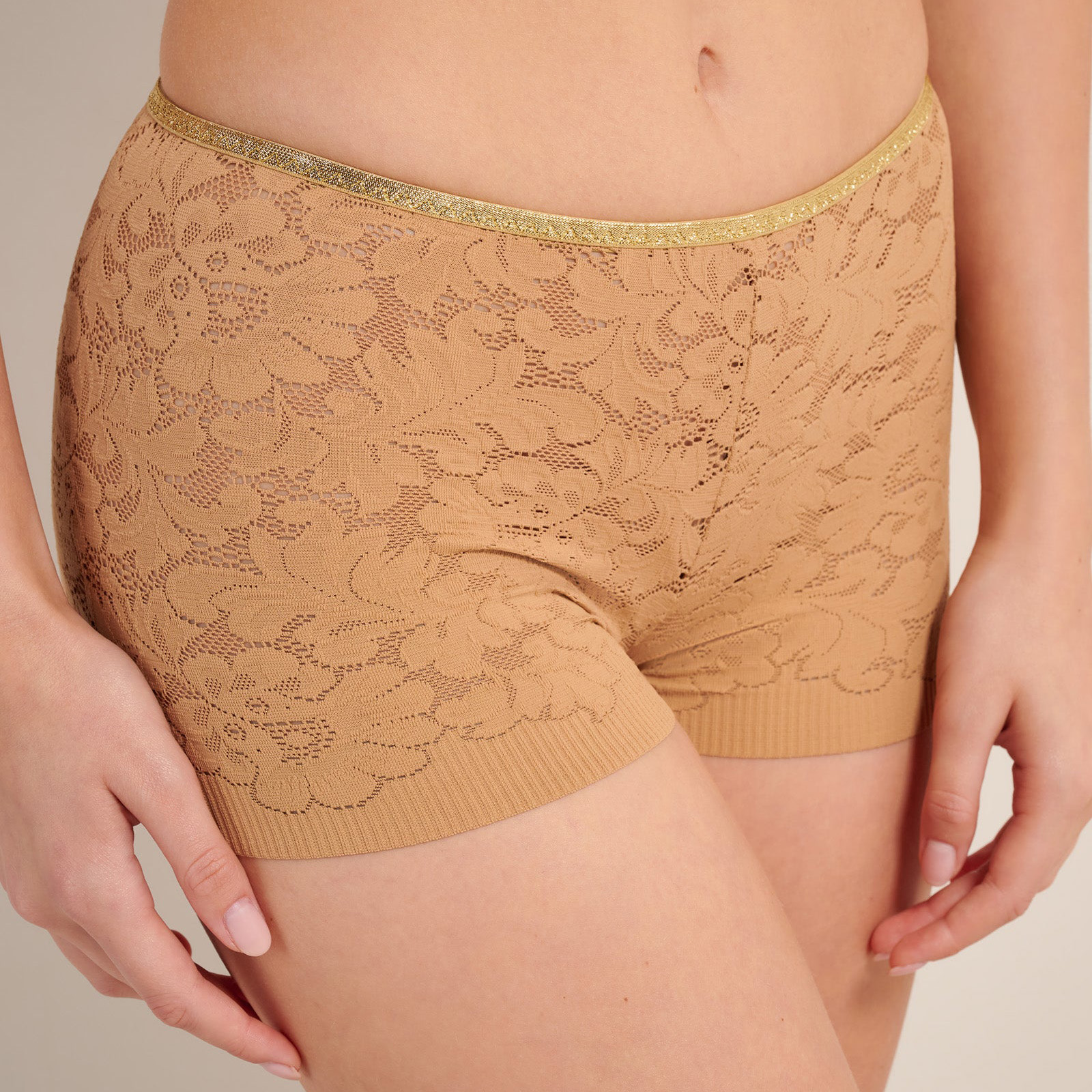 Cuecas de renda bege com padrão floral e cós dourado em modelo