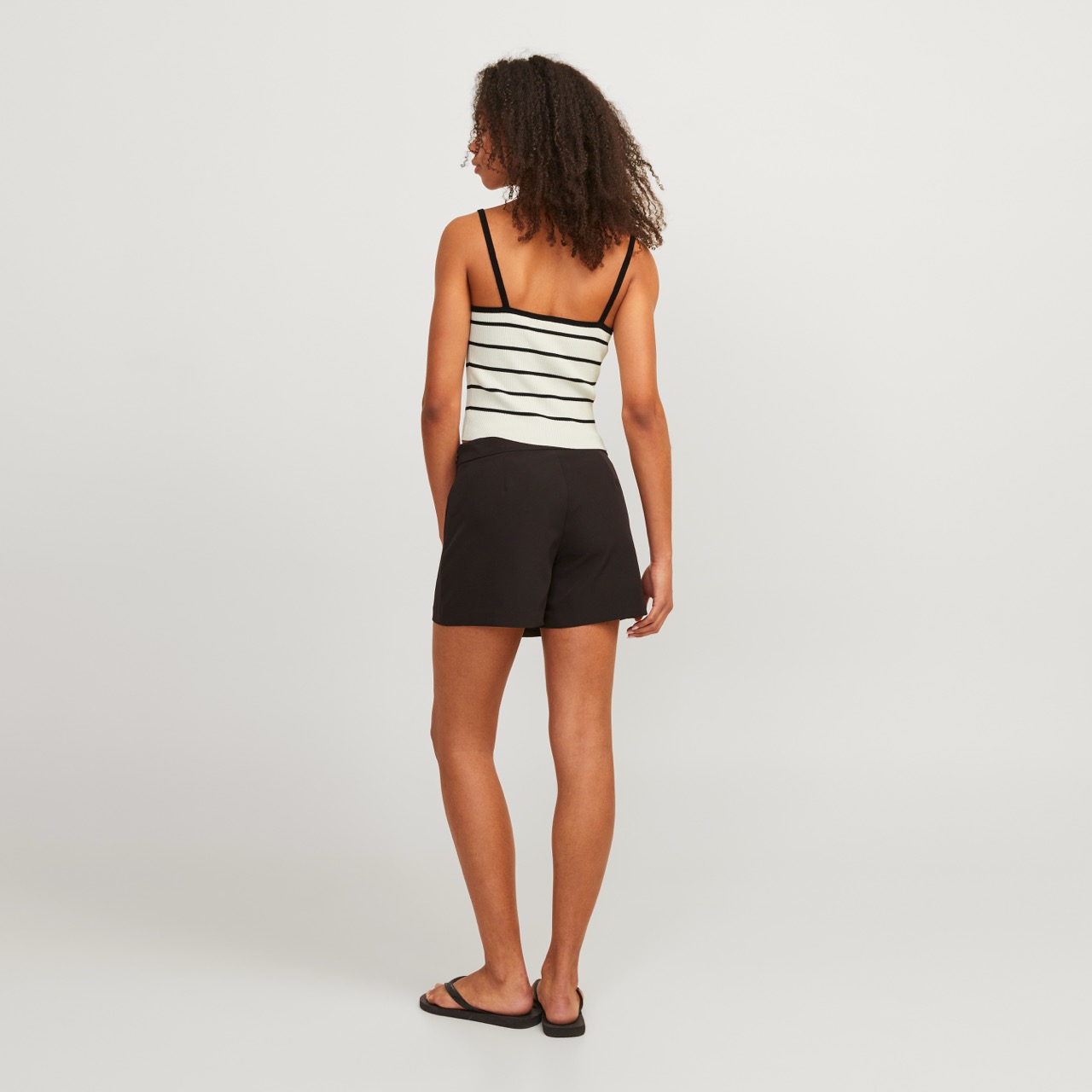 Mulher de costas com top riscado branco e preto e calções pretos