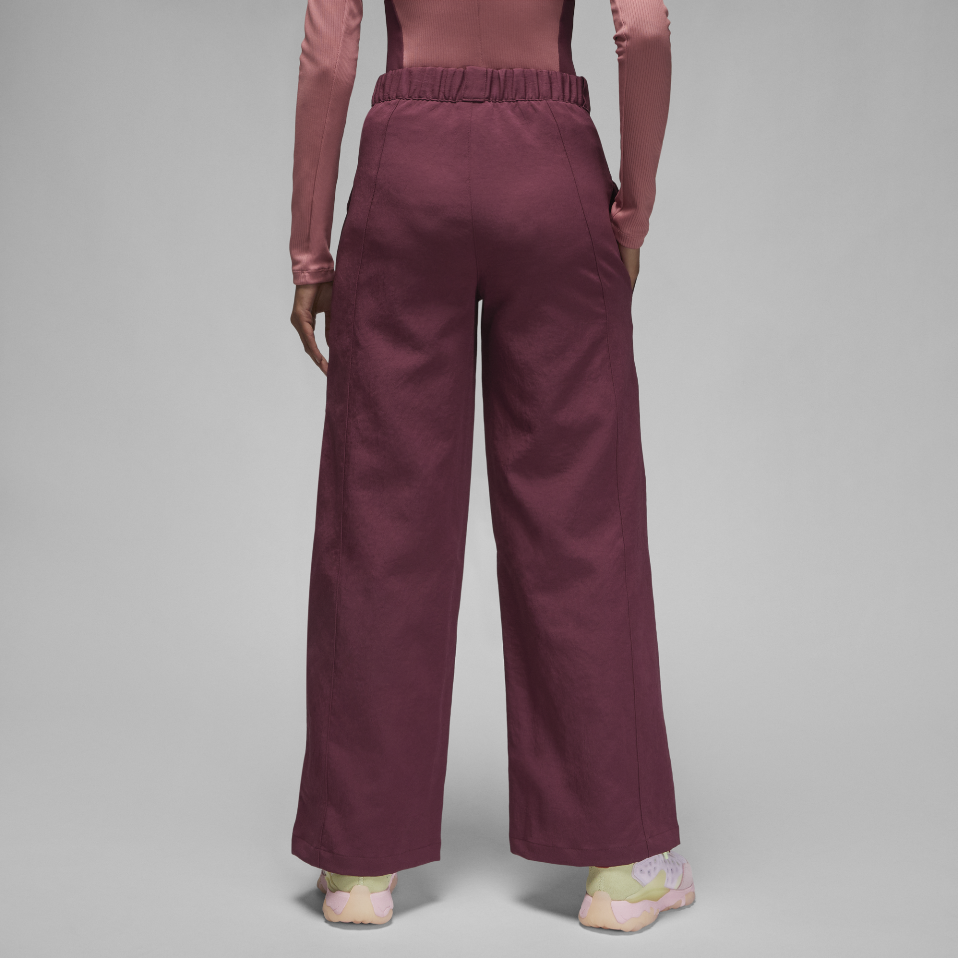 Calças largas vinho de cintura elástica vistas de trás com top rosa e sapatilhas multicoloridas