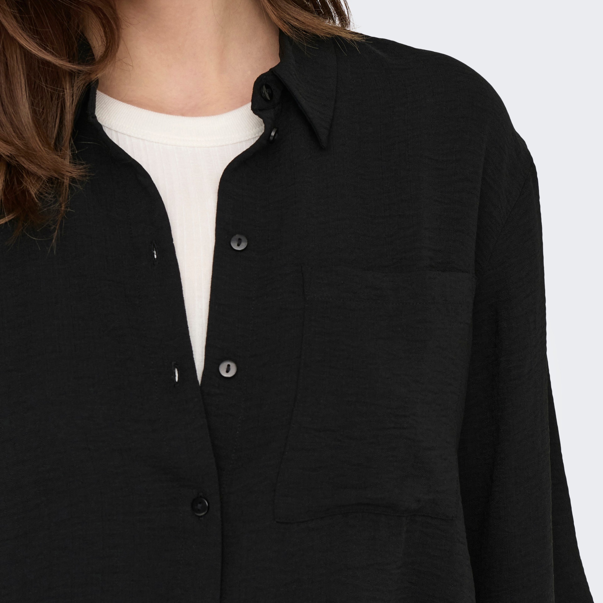 Camisa preta com bolso frontal e botões pretos usada sobre t-shirt branca