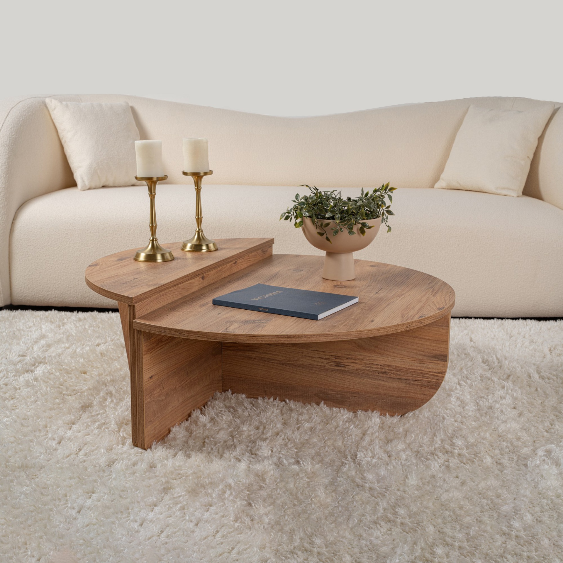 Mesa de centro em madeira clara com castiçais, vaso e livro em sala com sofá creme.