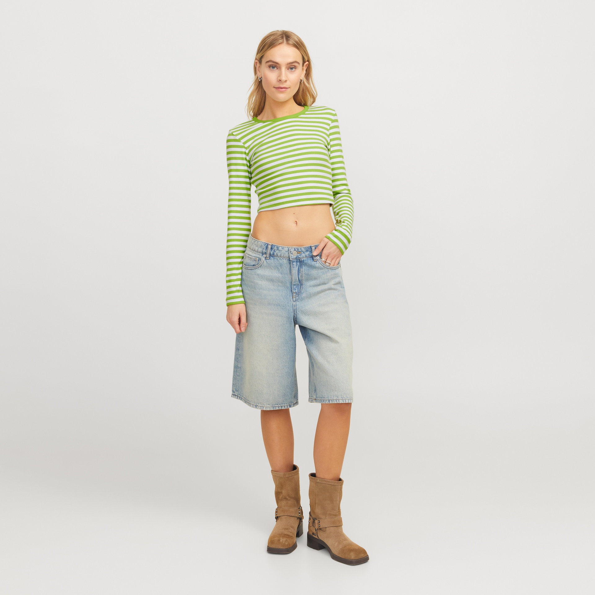 Mulher com top riscado verde e branco, bermuda de ganga azul clara e botas castanhas