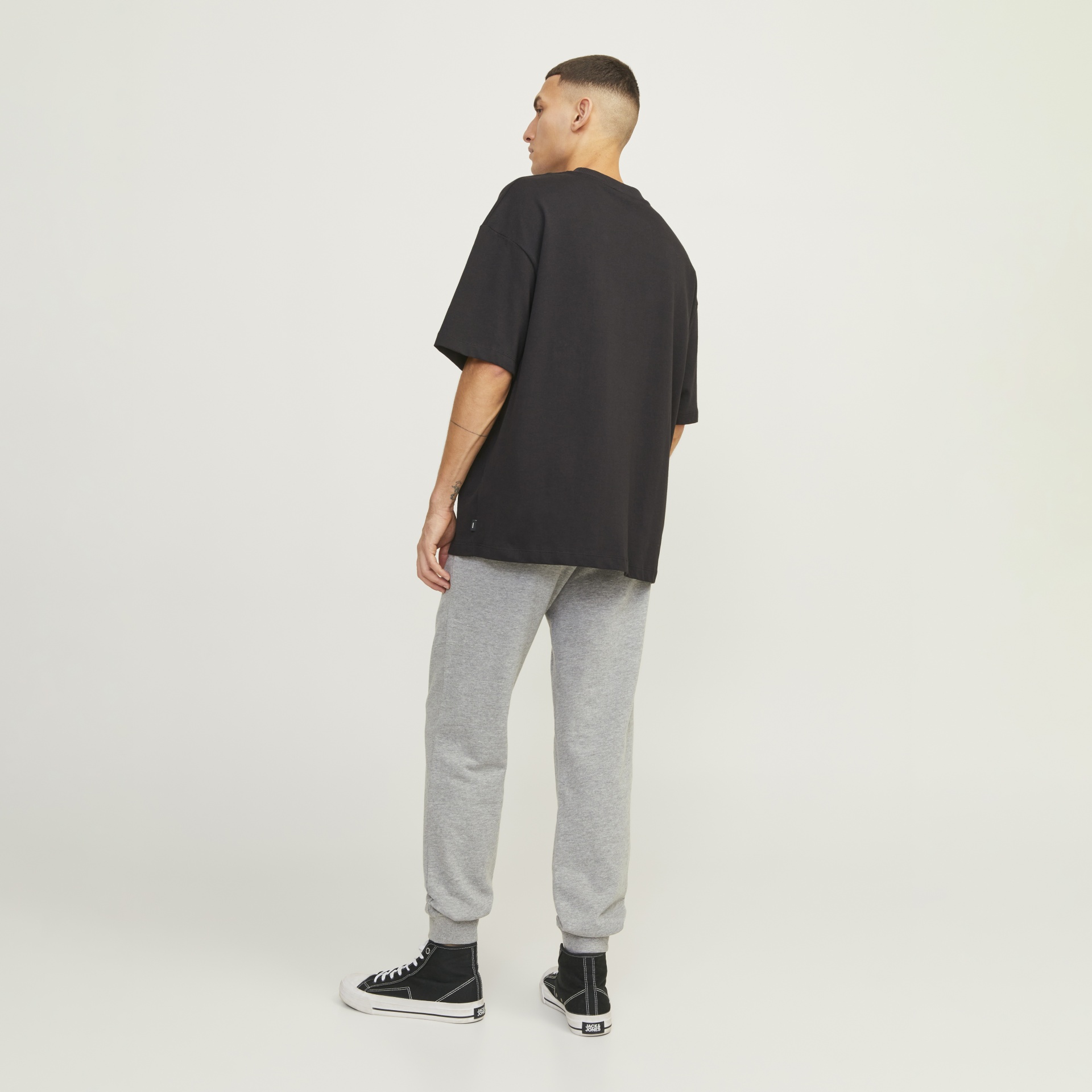 Homem de costas com t-shirt preta, calças cinza e ténis pretos e brancos JACK & JONES