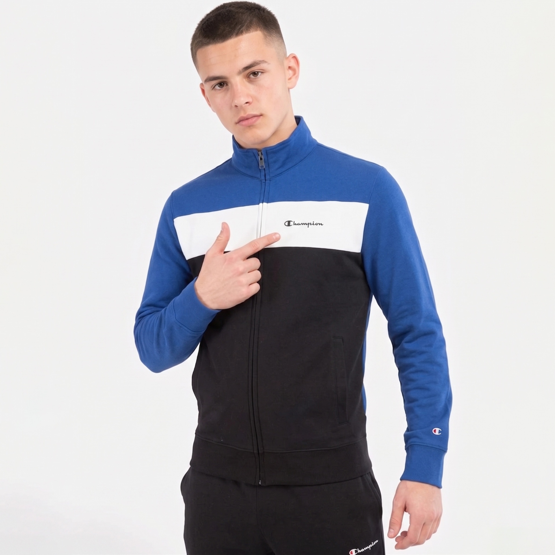 Homem a usar casaco e calças desportivas Champion, casaco azul, branco e preto.