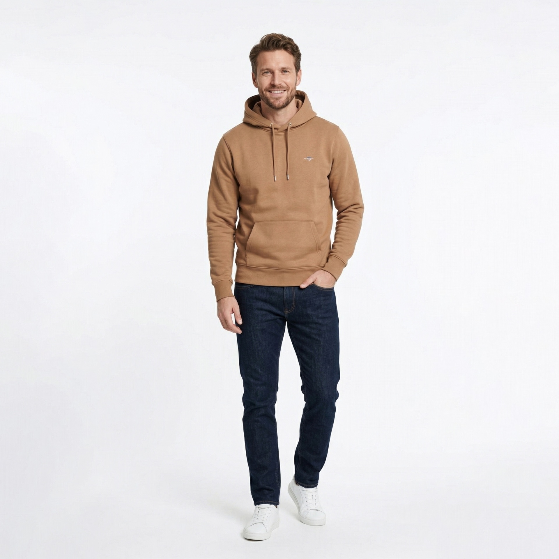 Homem com hoodie castanho, jeans azul escuro e sapatilhas brancas.