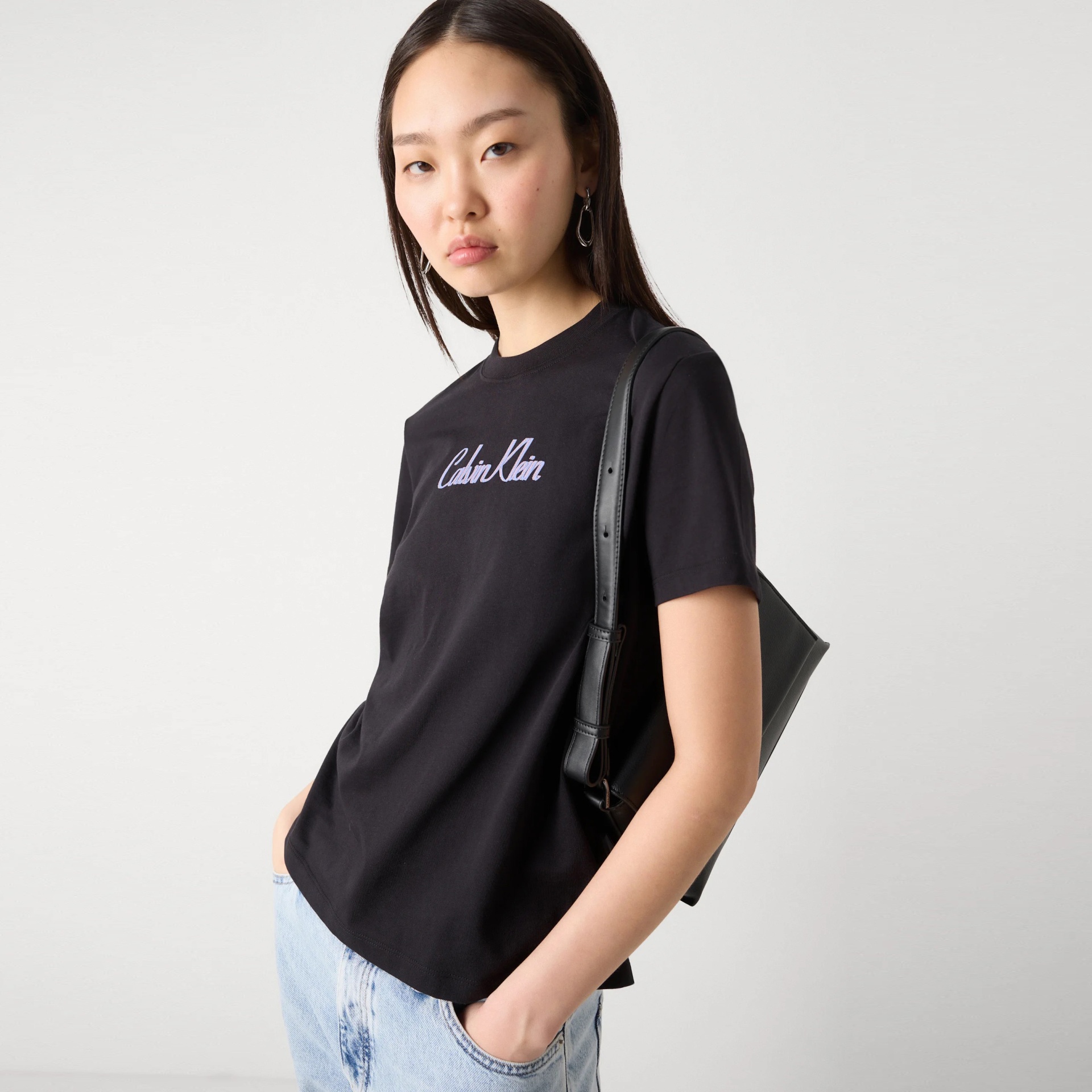 Mulher com t-shirt preta Calvin Klein, calças de ganga claras e mala preta ao ombro