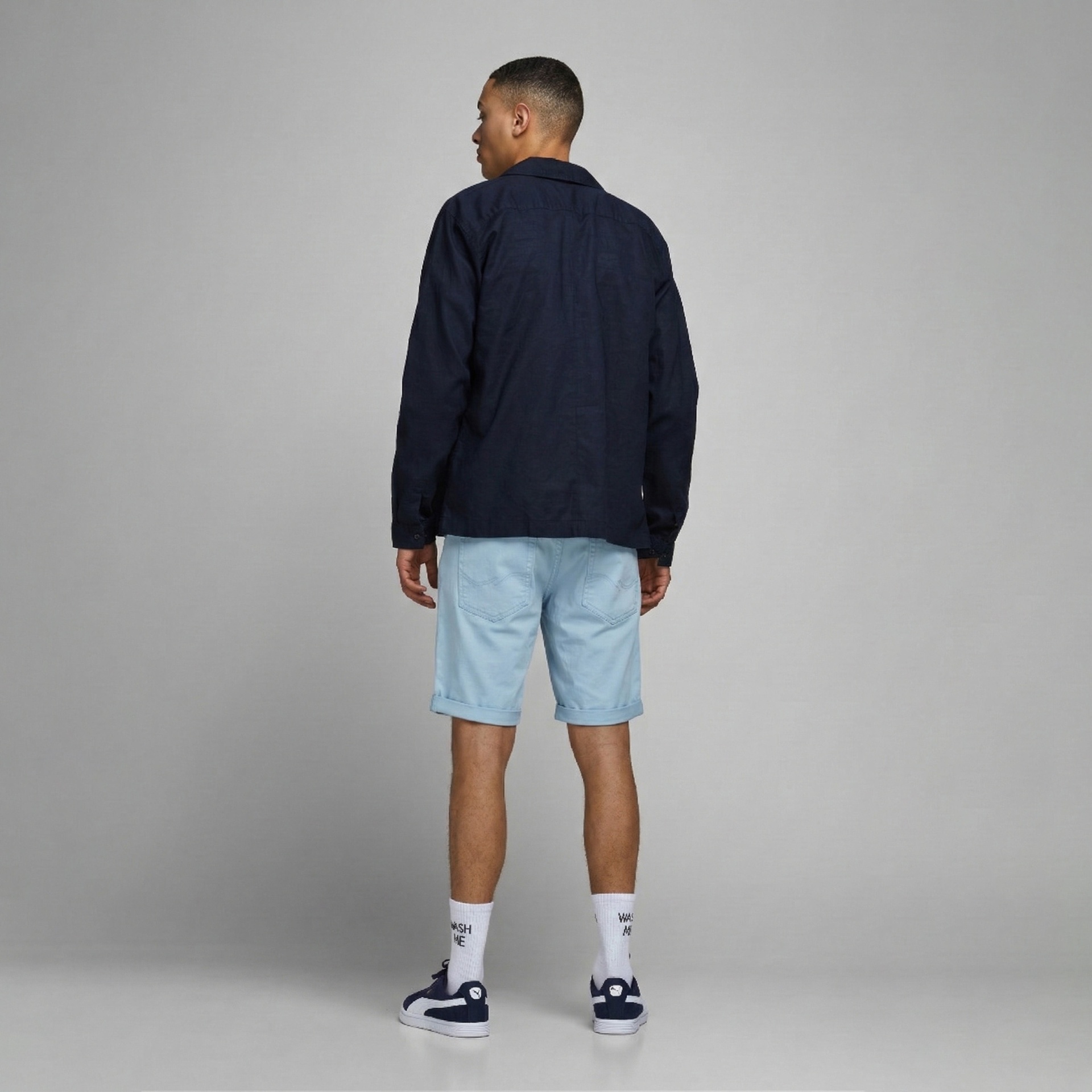 Homem com camisa azul escura, calções de ganga azul e sapatilhas azuis, visto de costas