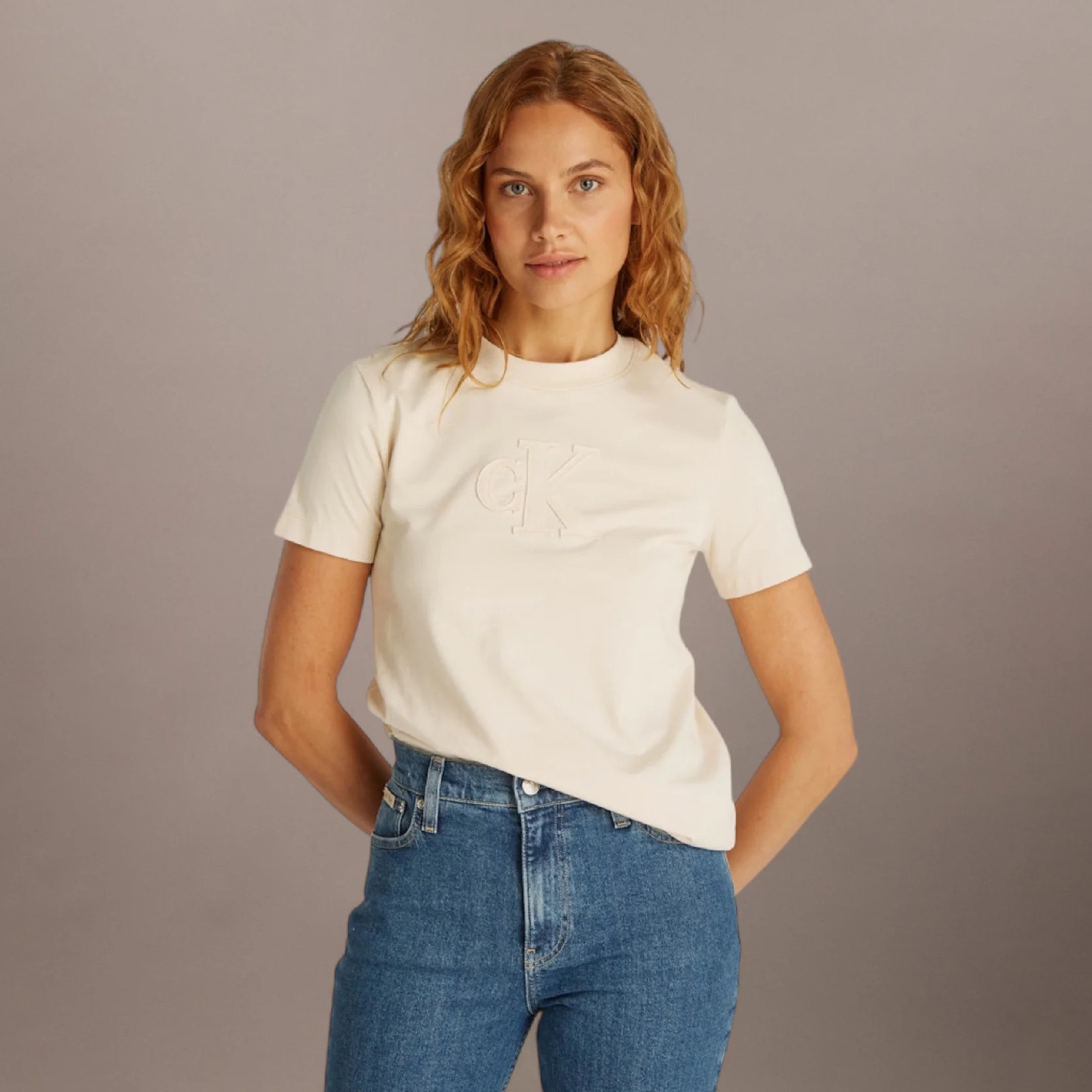 Mulher com t-shirt creme com logo ck em relevo e jeans azul claro