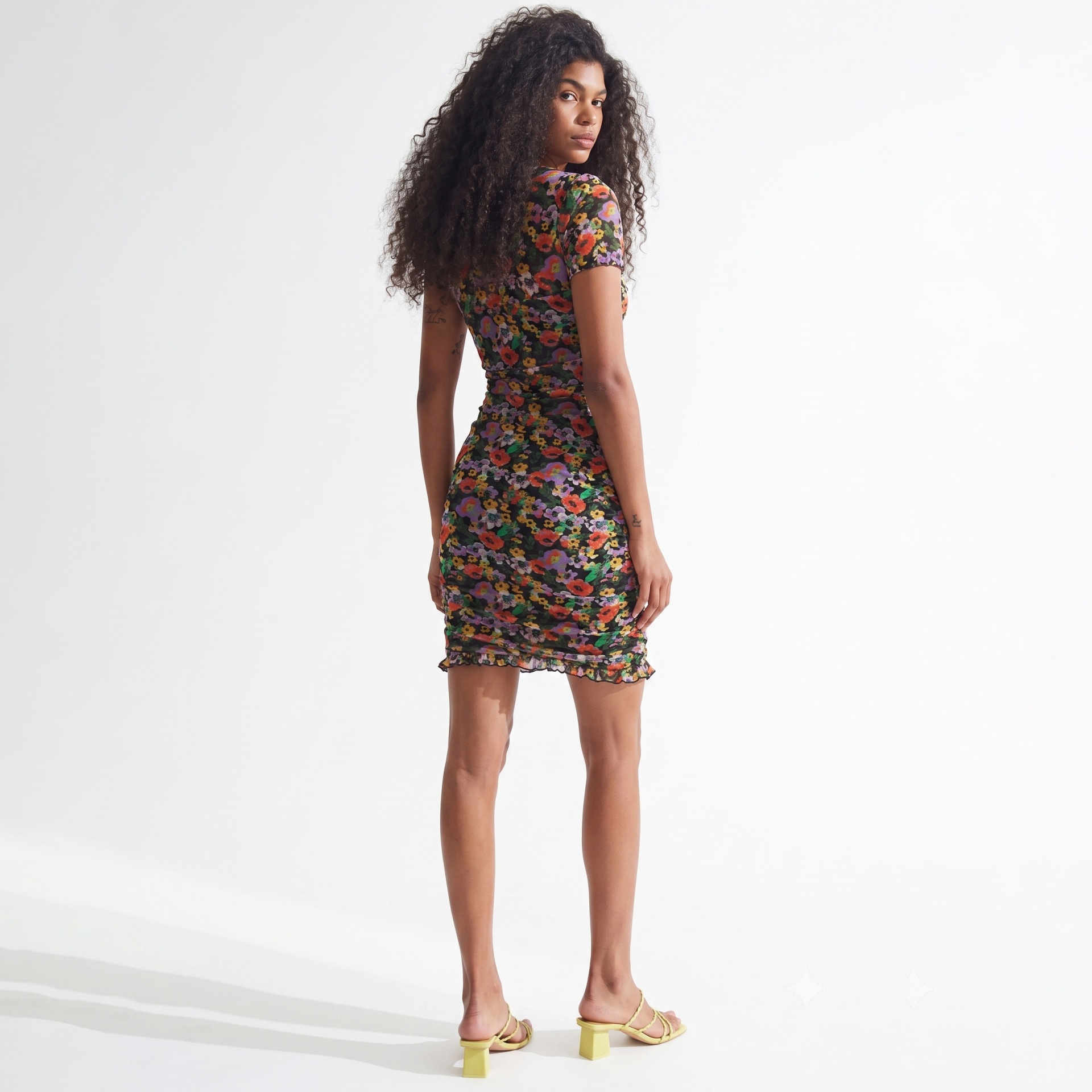 Vestido curto justo com padrão floral colorido em fundo preto e sandálias amarelas de salto