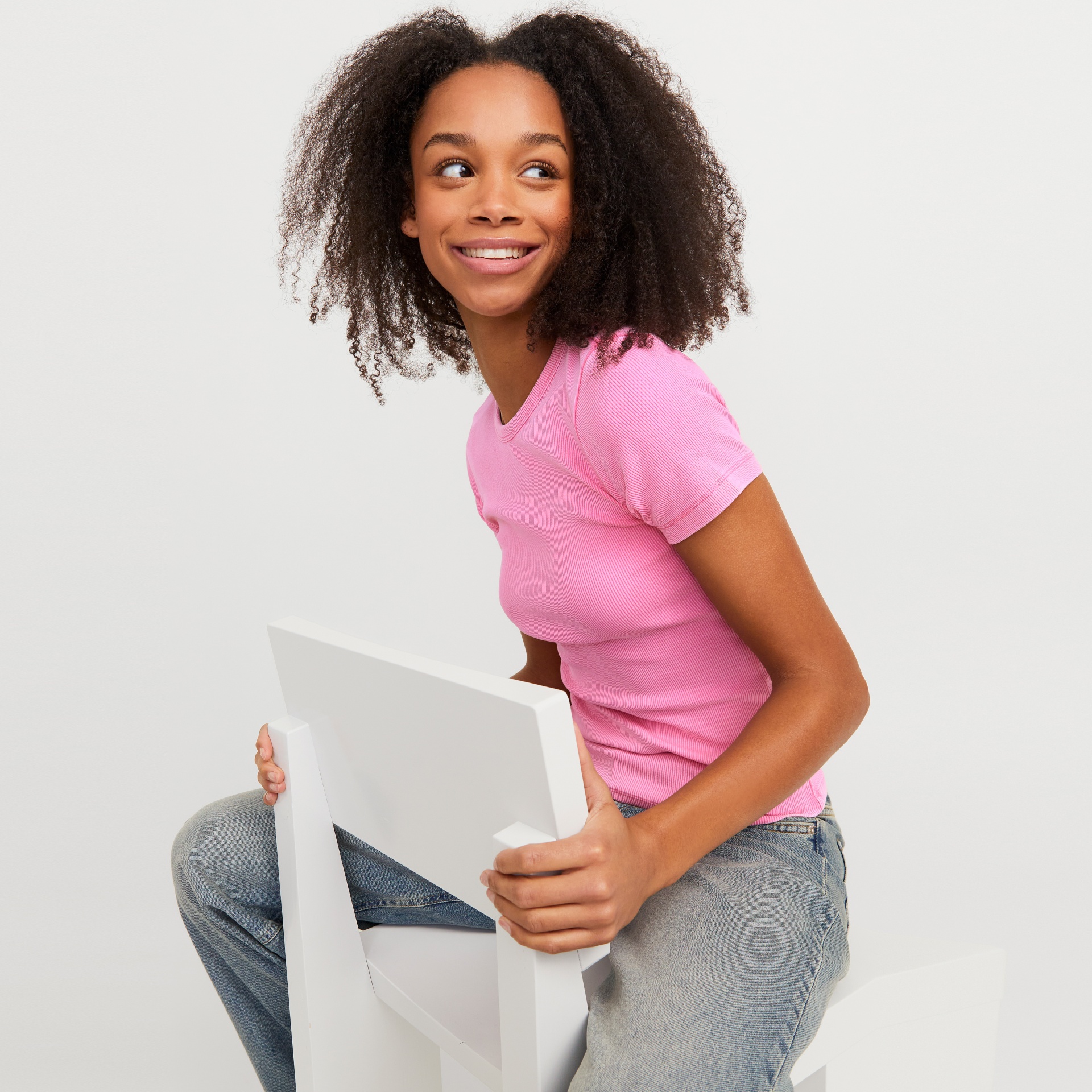 Mulher com t-shirt rosa e calças de ganga sentada numa cadeira branca