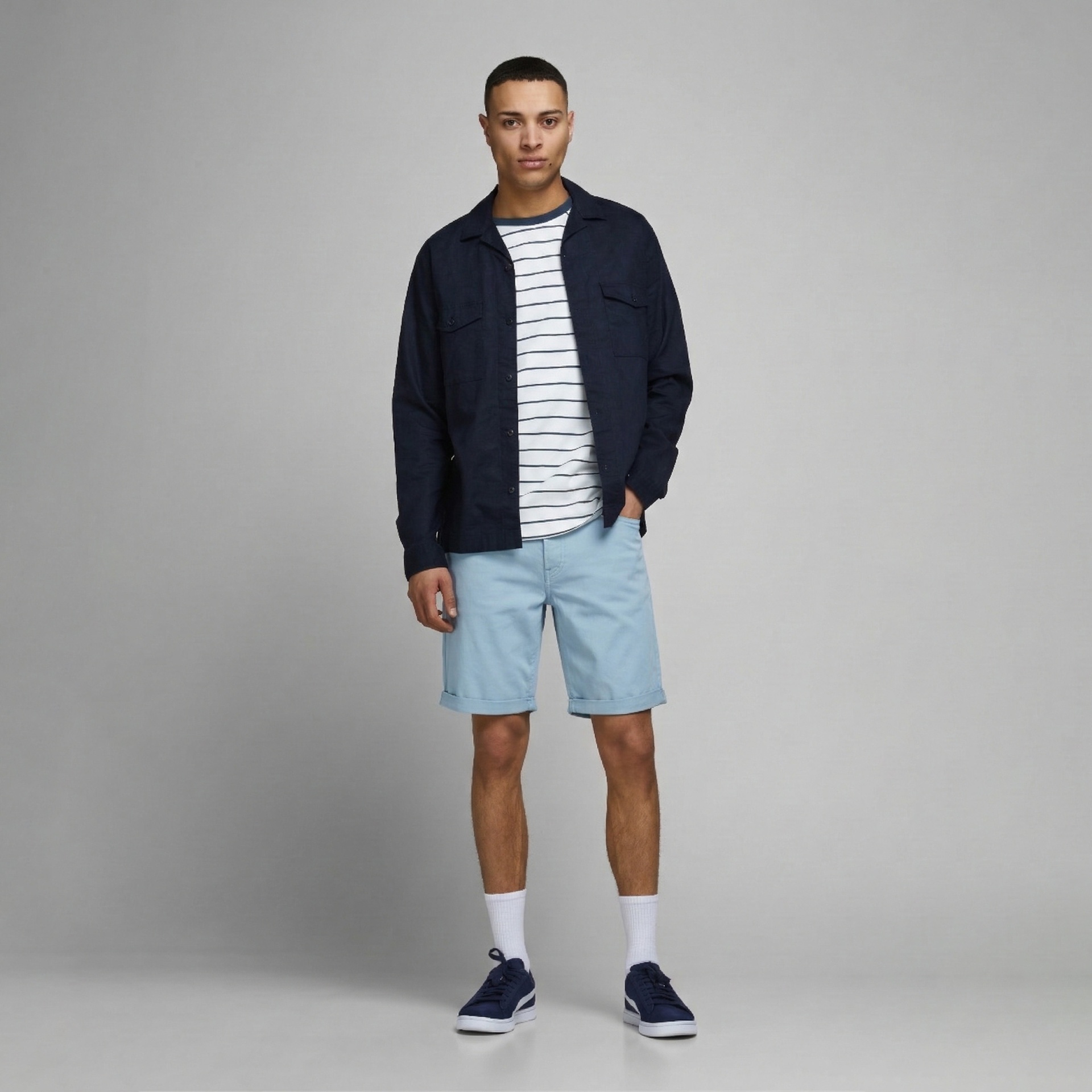 Homem com camisa azul escura, t-shirt às riscas, calções azuis claros e ténis azuis.