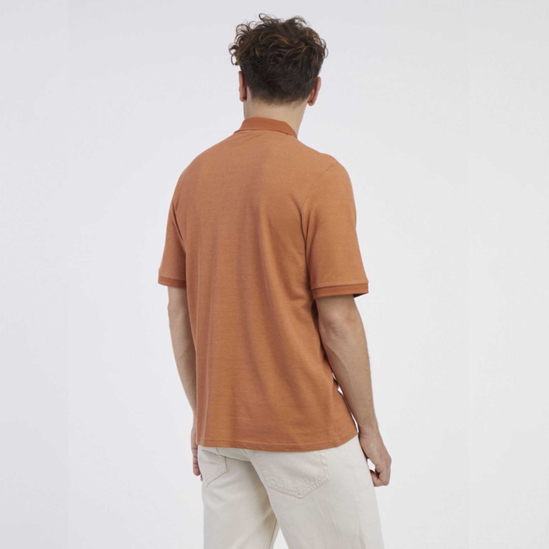 Homem de costas com camisola tipo polo cor ferrugem e calças claras