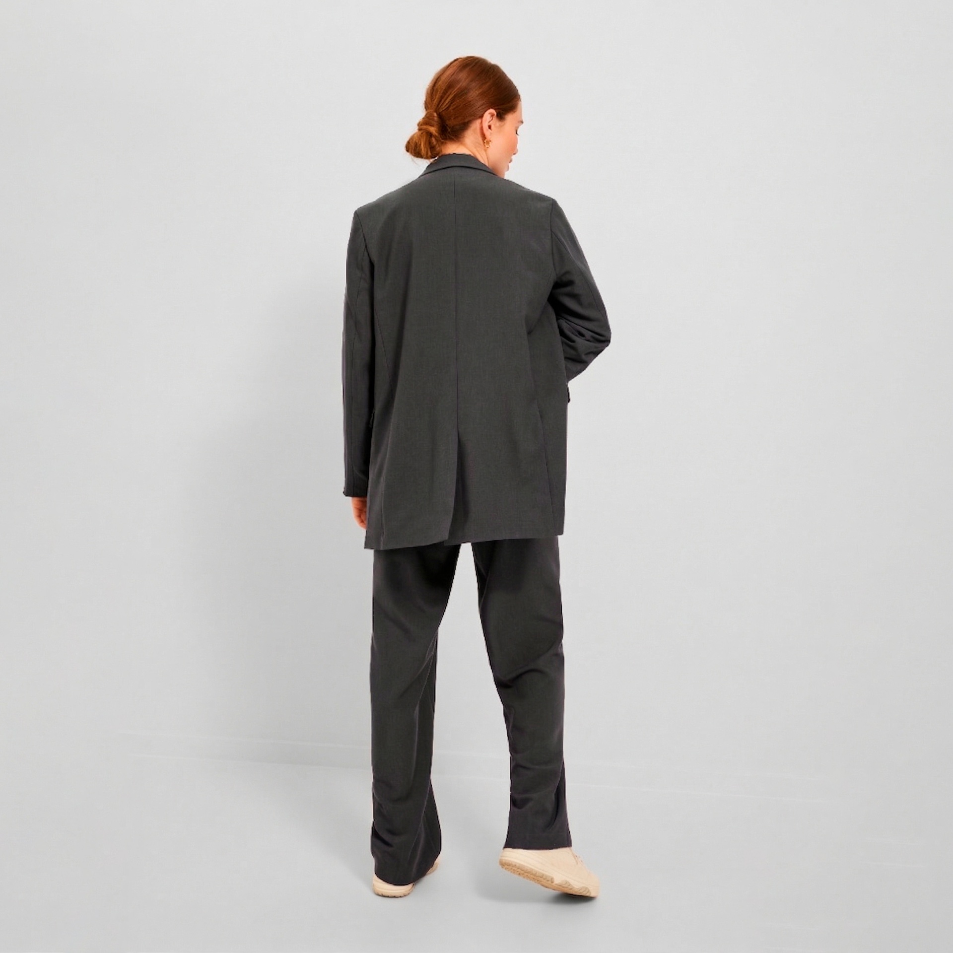Pessoa de costas com fato cinza escuro e sapatos claros em fundo branco.