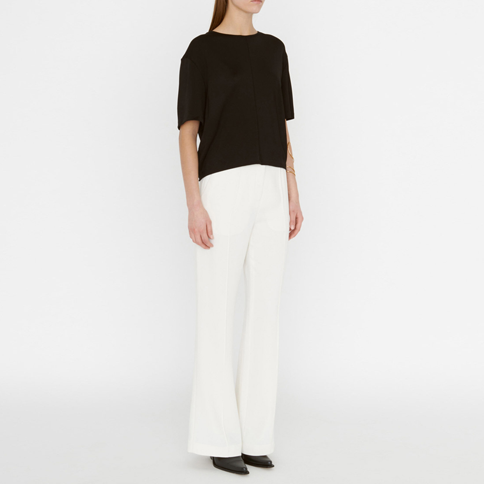 Mulher a vestir calças brancas largas e camisa preta de manga curta, com sapatos pretos