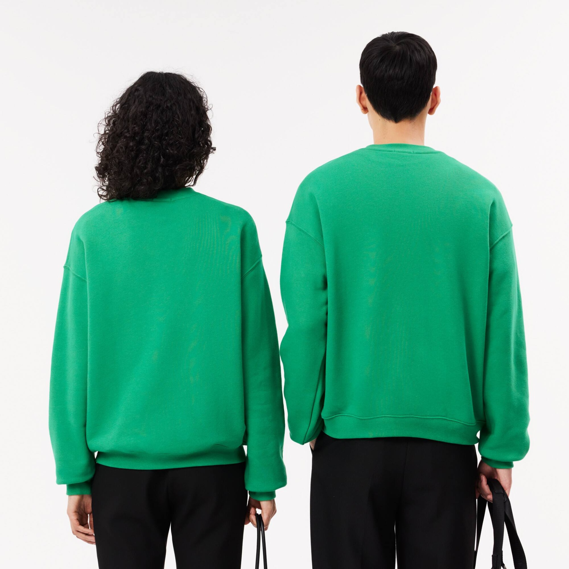 Duas pessoas de costas com sweatshirts verdes e calças pretas num fundo branco.