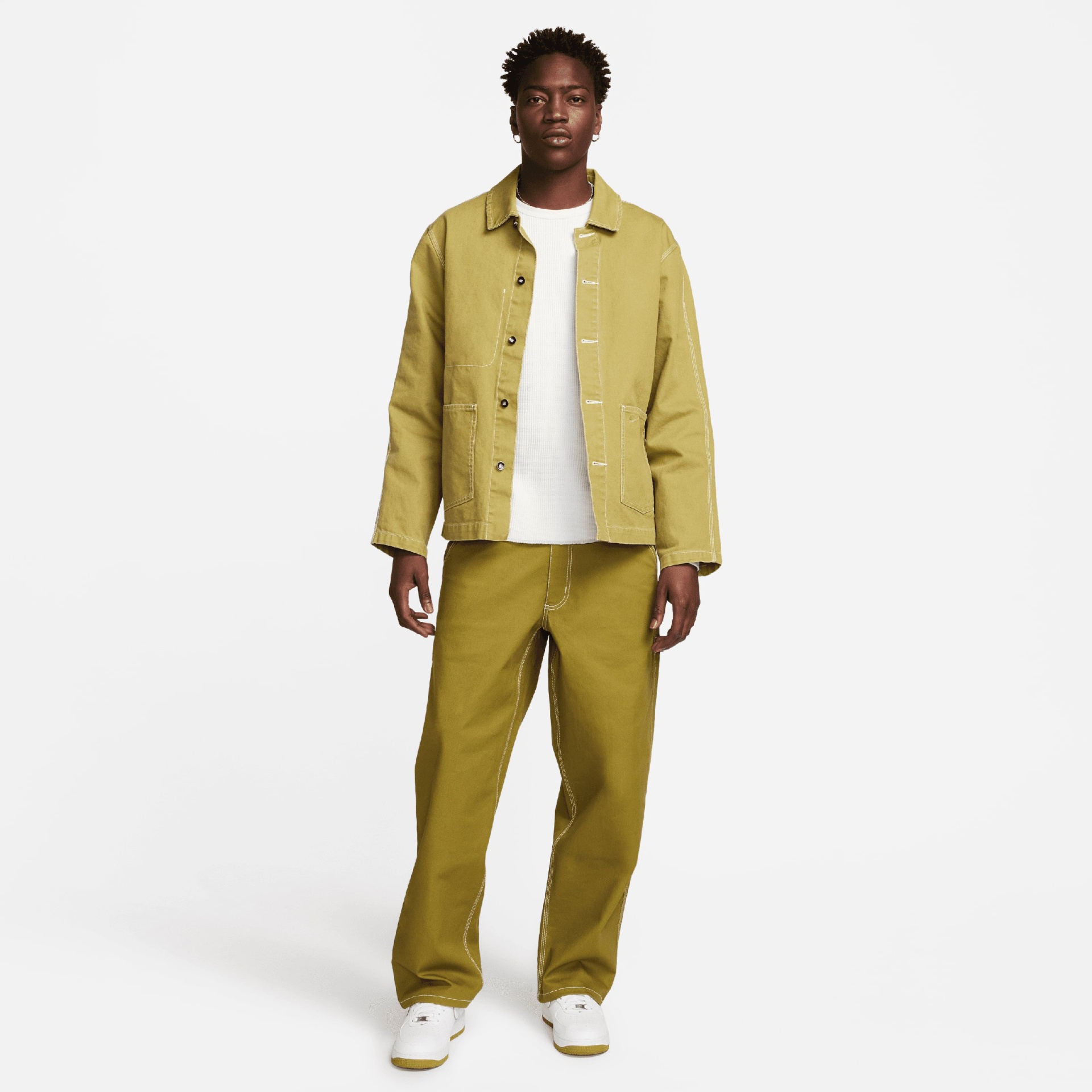 Homem com casaco e calças amarelo-oliva e sapatilhas brancas