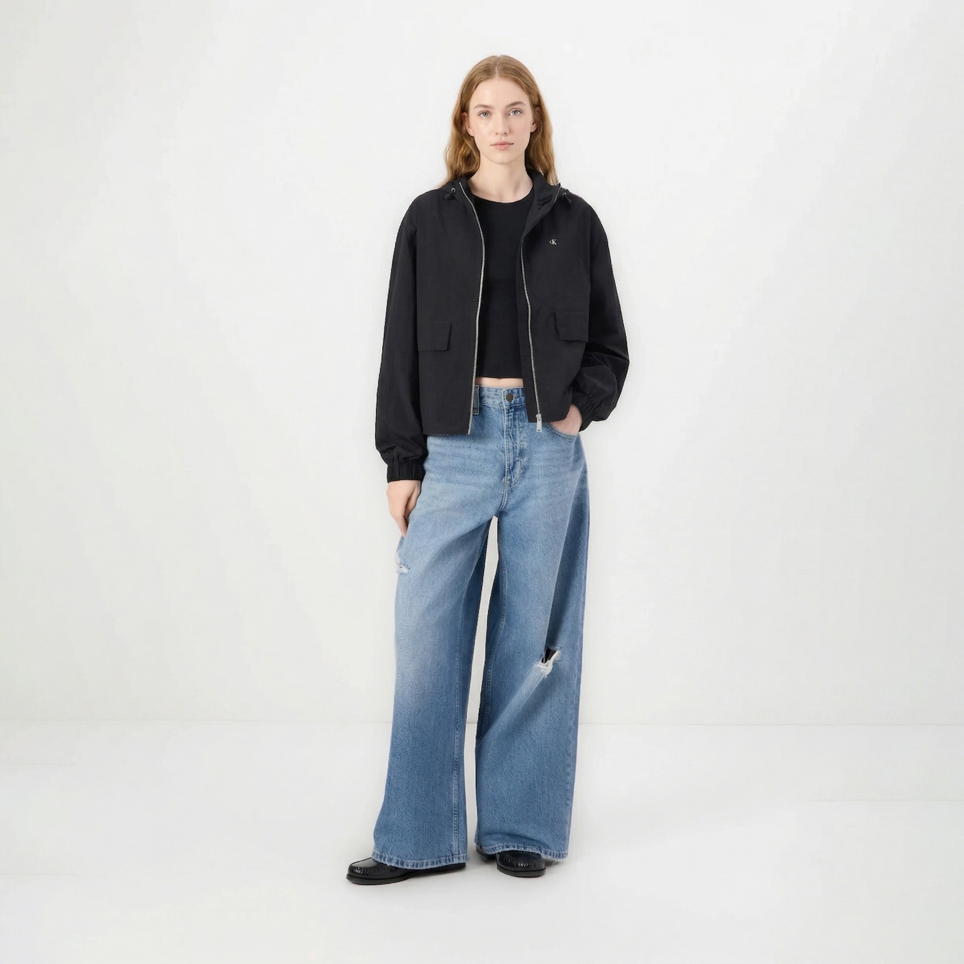 Mulher de pé com casaco preto e calças jeans largas