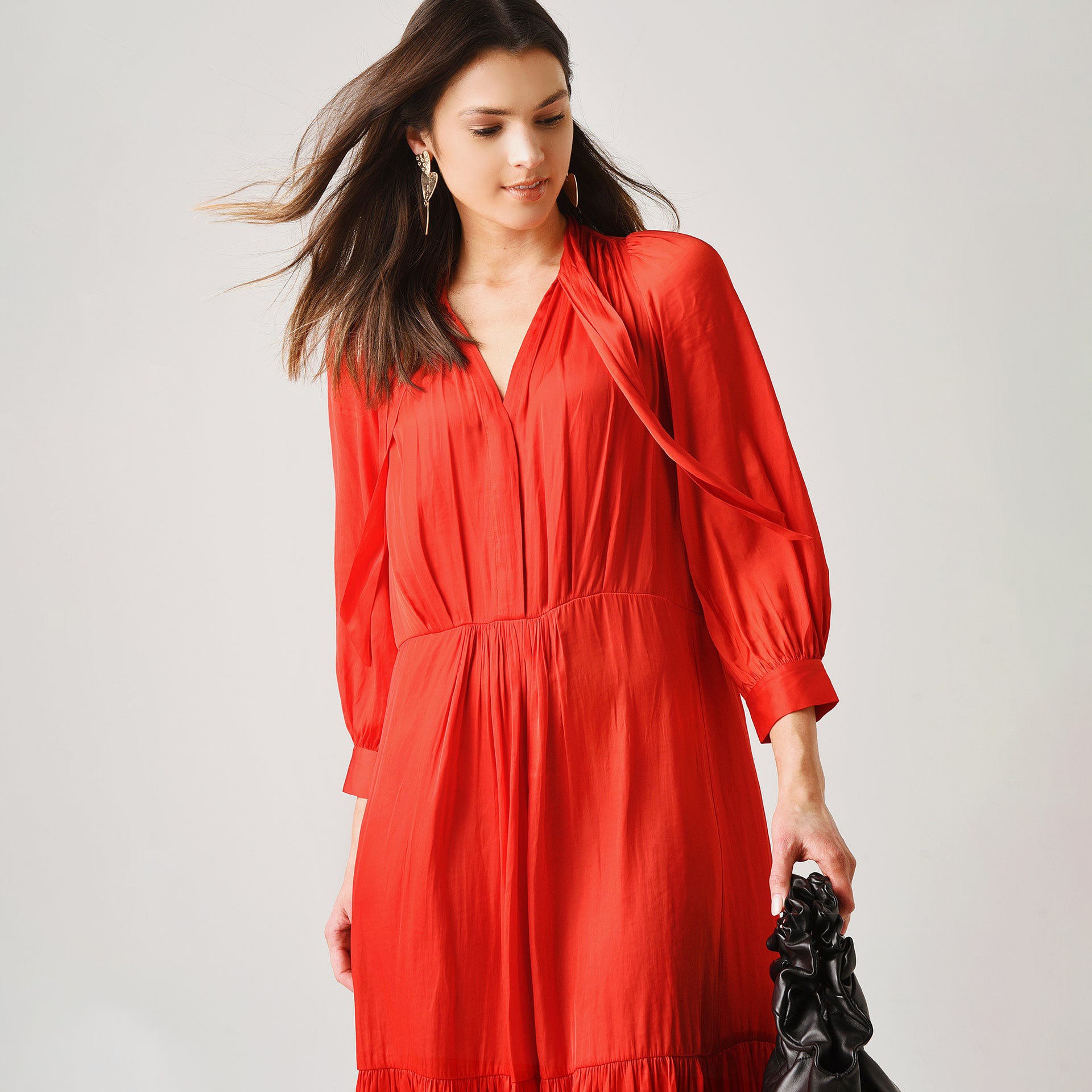 Vestido vermelho com mala preta e brinco dourado, fundo claro