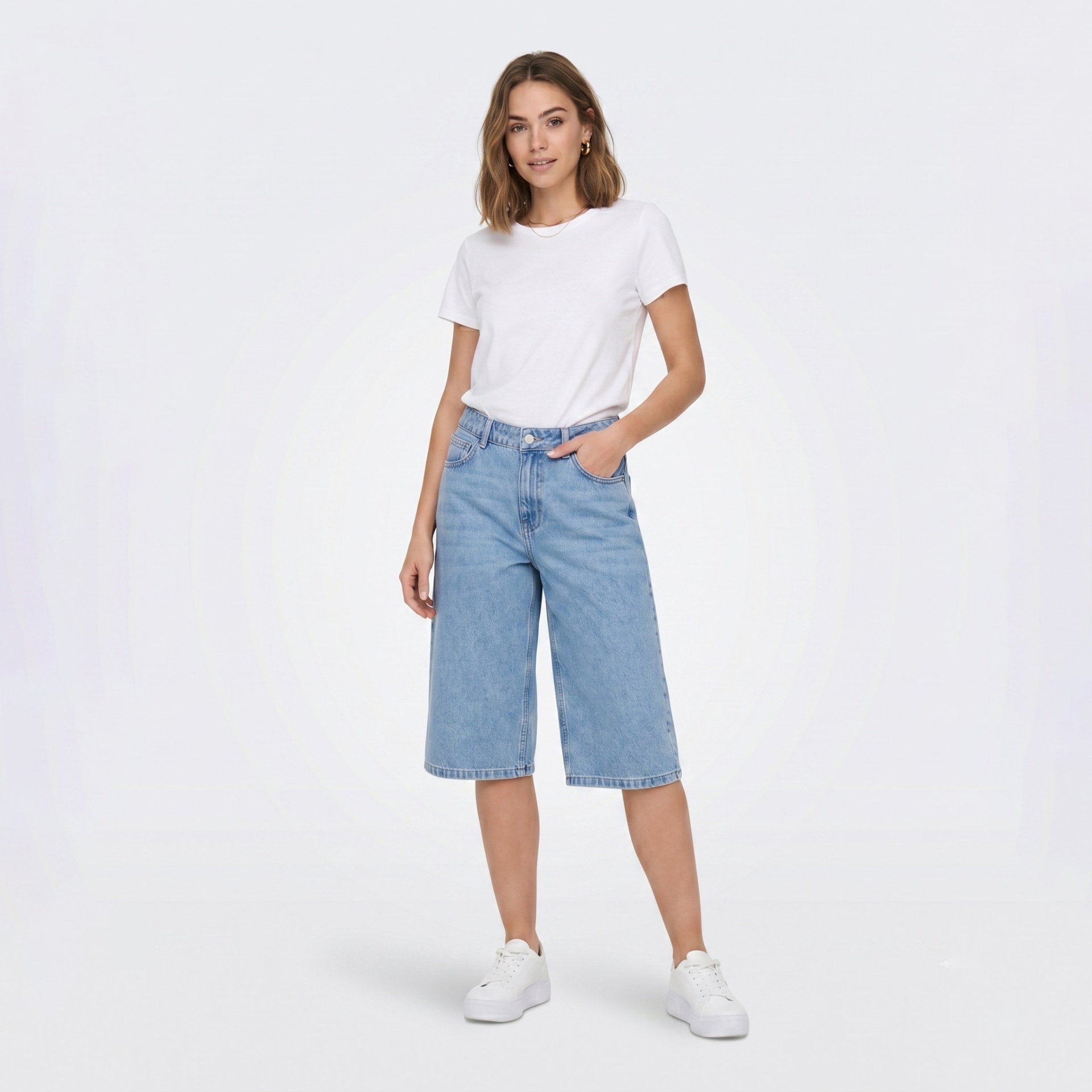 Modelo com calções de ganga compridos largos azul clara, t-shirt branca e sapatilhas brancas