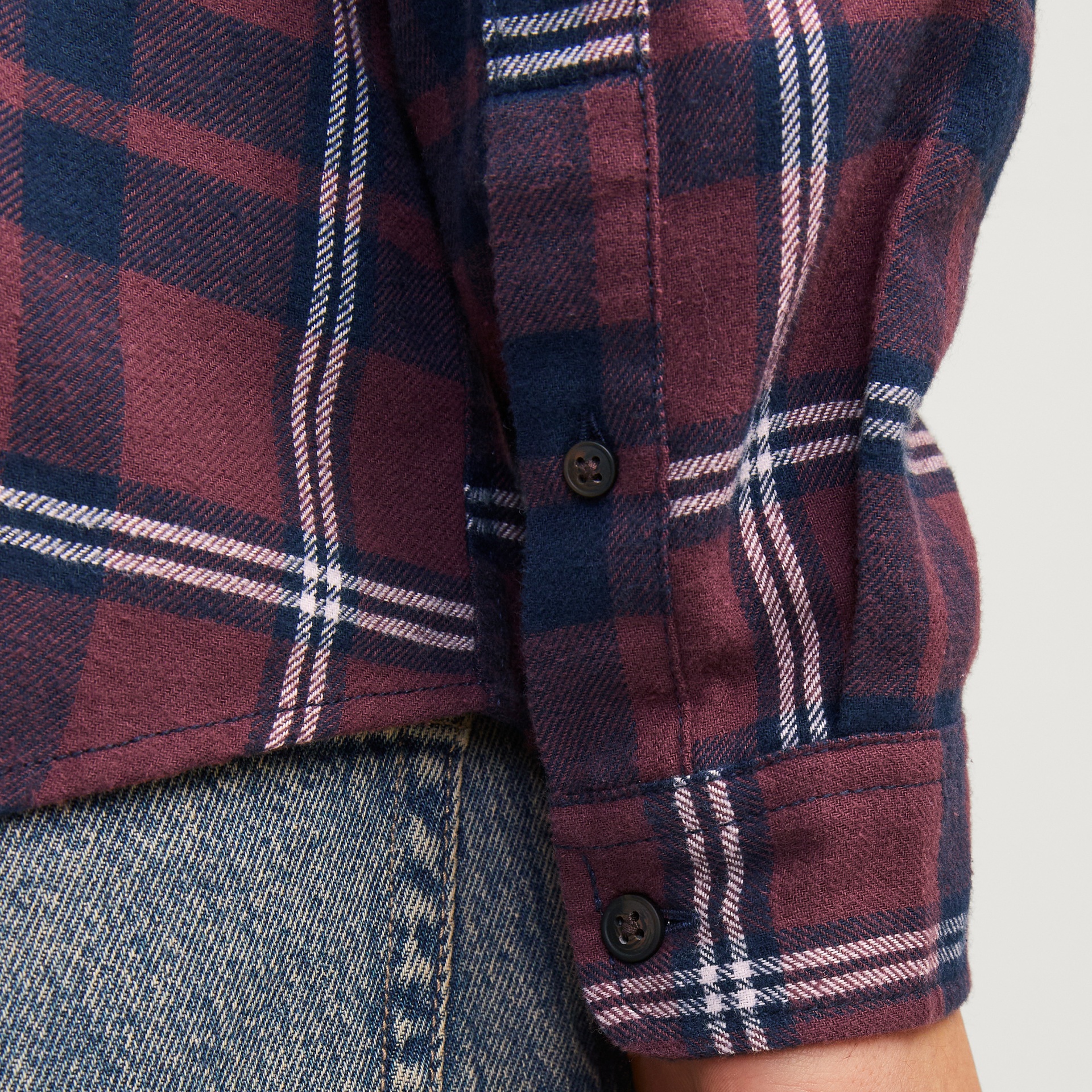 Manga de camisa xadrez bordo e azul com botões preta junto a calças de ganga