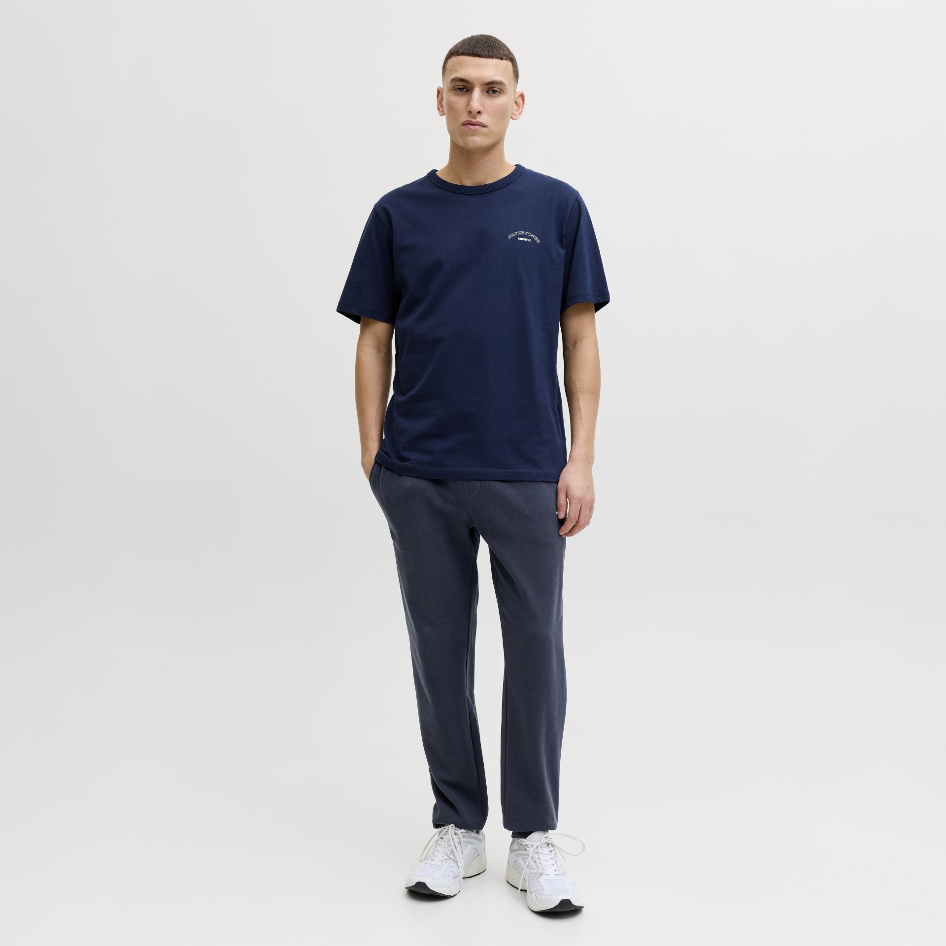 Homem com t-shirt azul escura, calças azul-escuras e tênis brancos