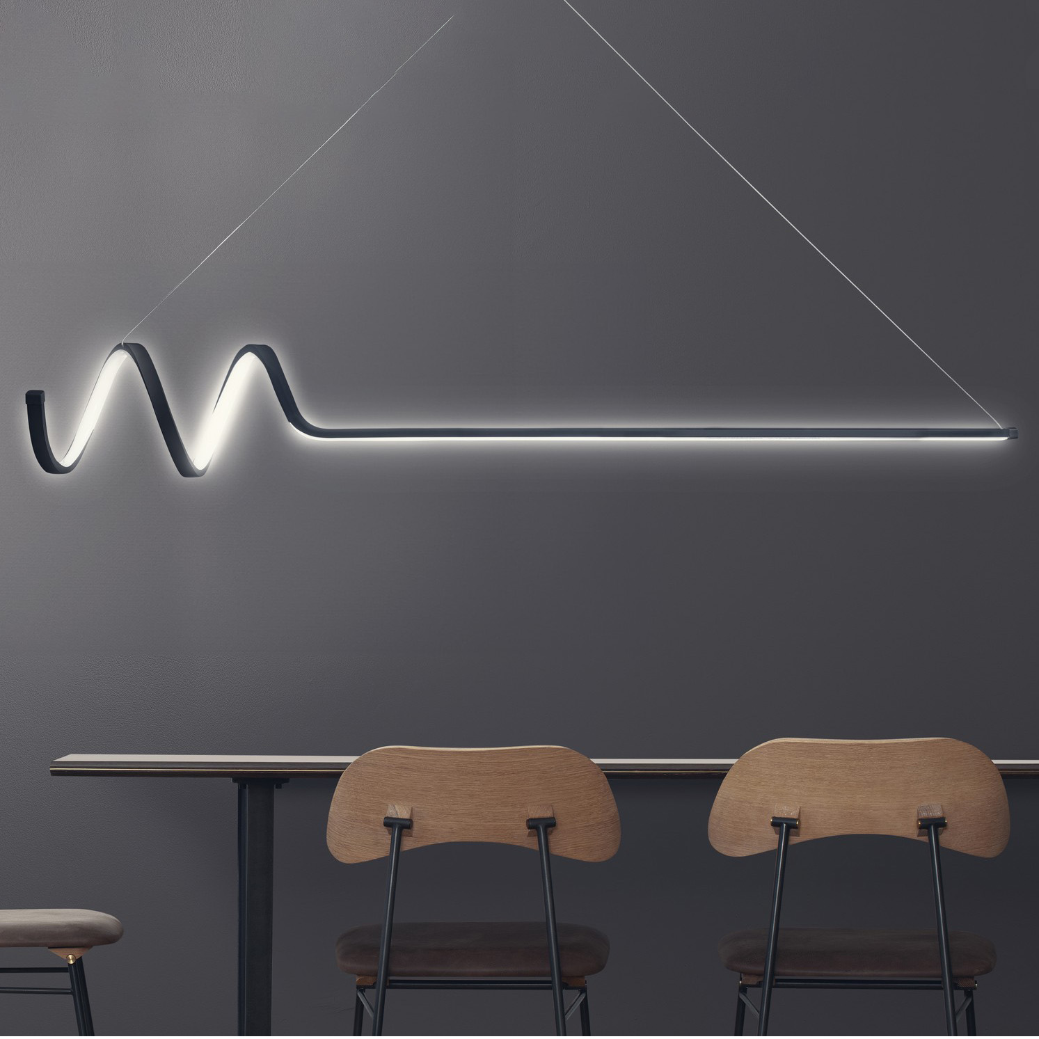 Luminária LED branca ondulada numa parede cinza acima de mesa com cadeiras de madeira e metal