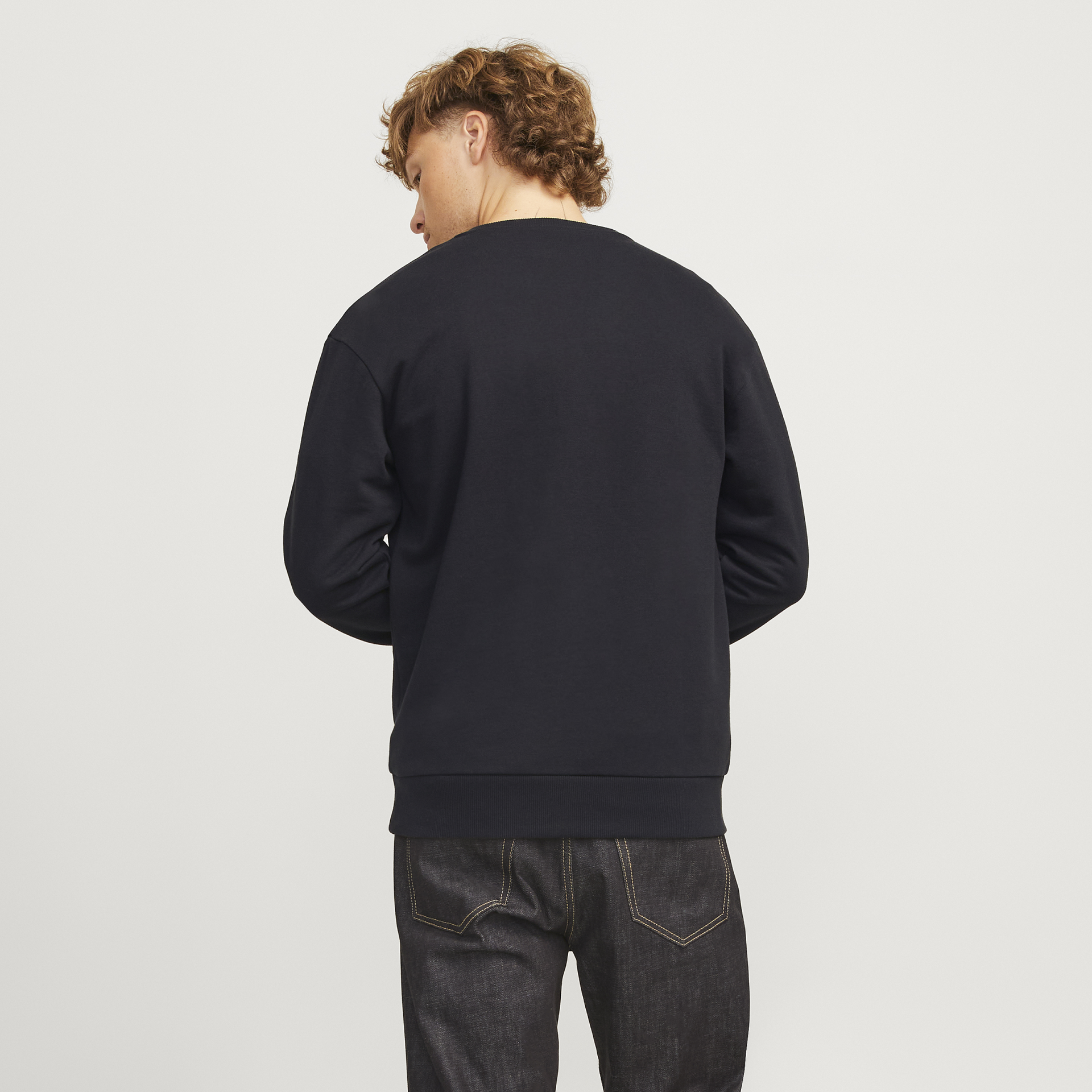 Homem de costas com sweatshirt preta e jeans escuros