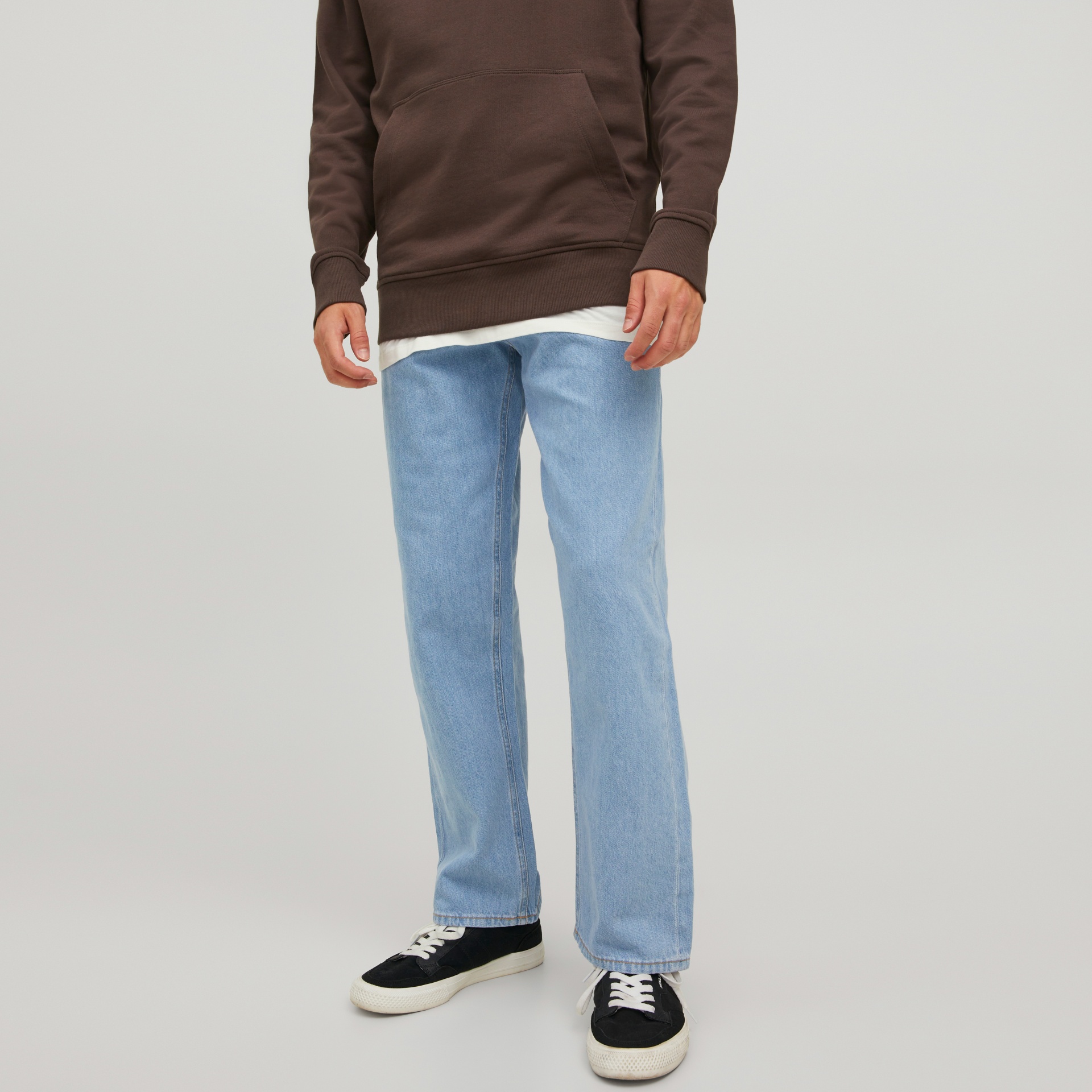 Homem com calças de ganga azuis, ténis pretos e sweat castanha