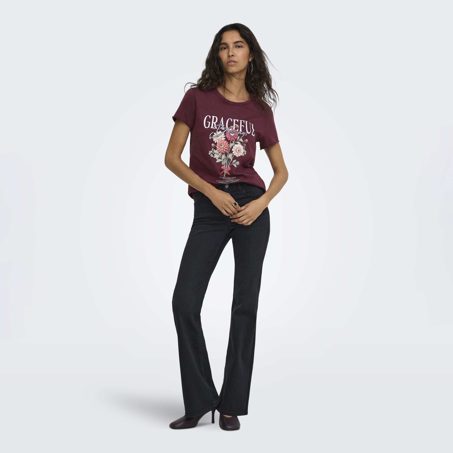Mulher vestindo t-shirt bordeaux com estampa floral e texto, calças jeans pretas e sapatos de salto