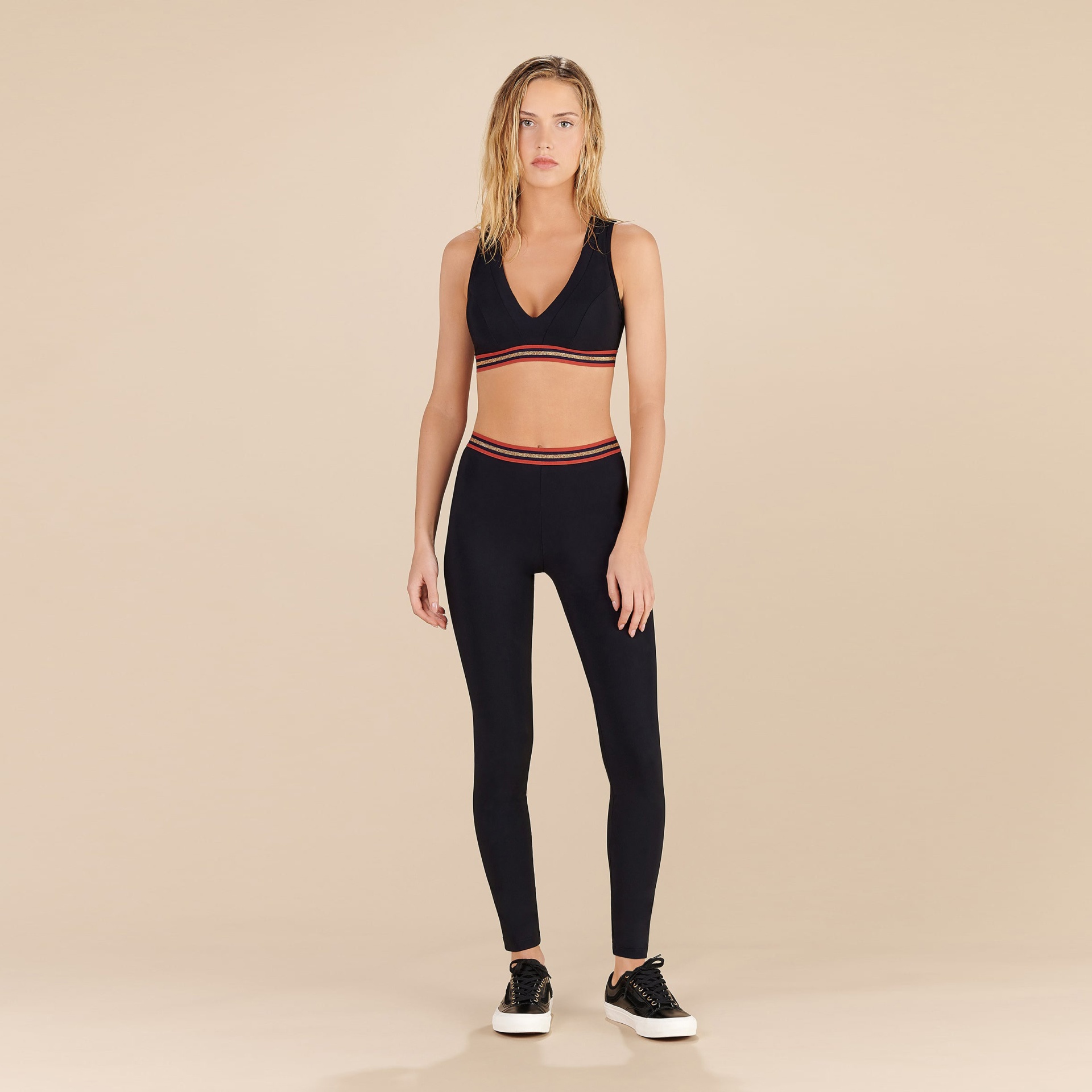 mulher com conjunto de roupa desportiva preto com detalhes vermelhos e brancos em fundo bege