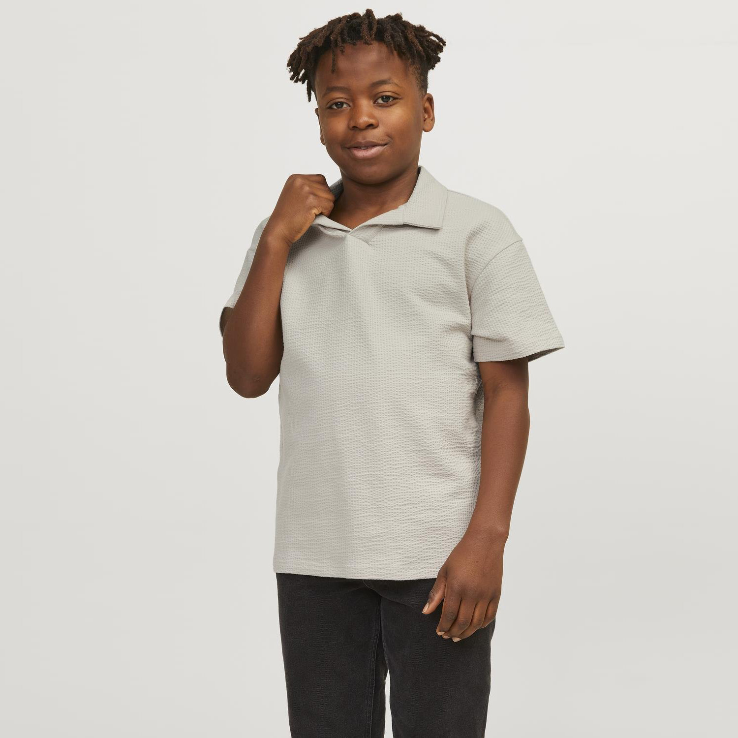 Criança vestindo camisola polo cinzenta clara texturizada com mangas curtas em fundo branco