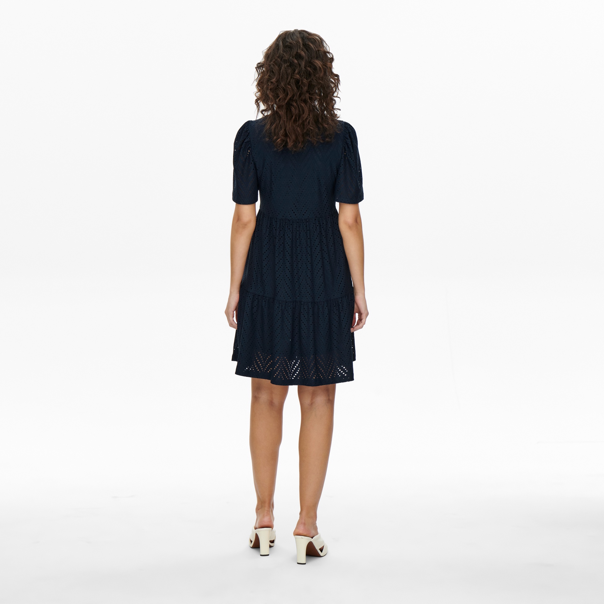 Vestido azul escuro com padrão vazado, mulher vista de costas com sandálias brancas.