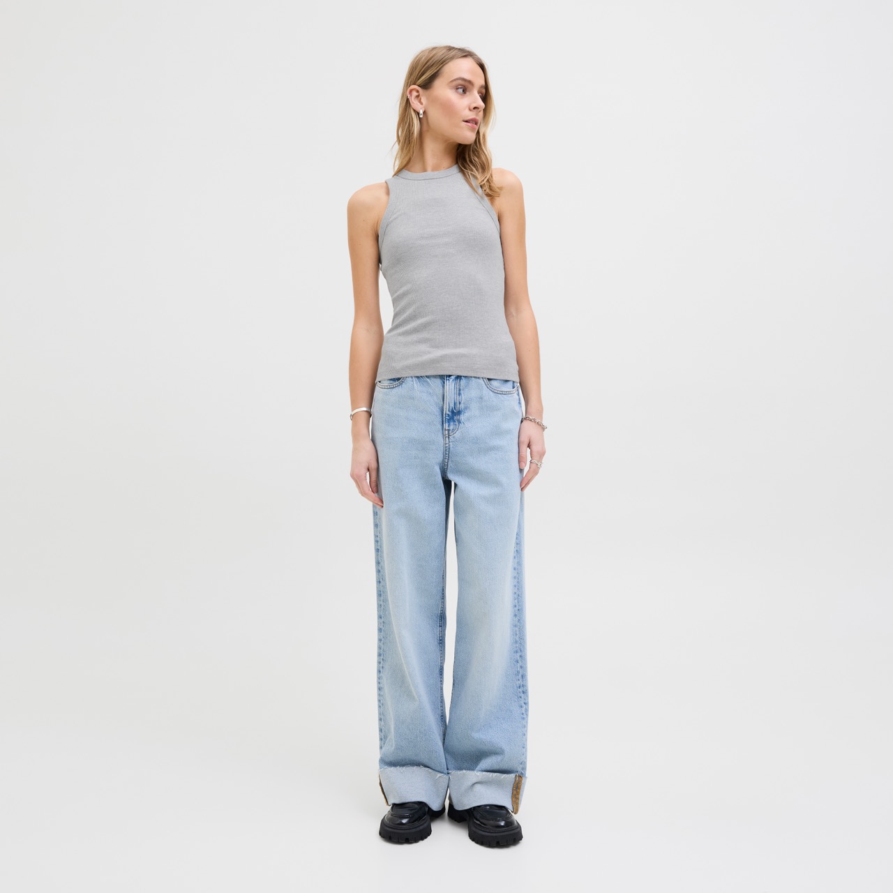 Mulher com top cinza de gola alta e calças largas de ganga claras em fundo branco