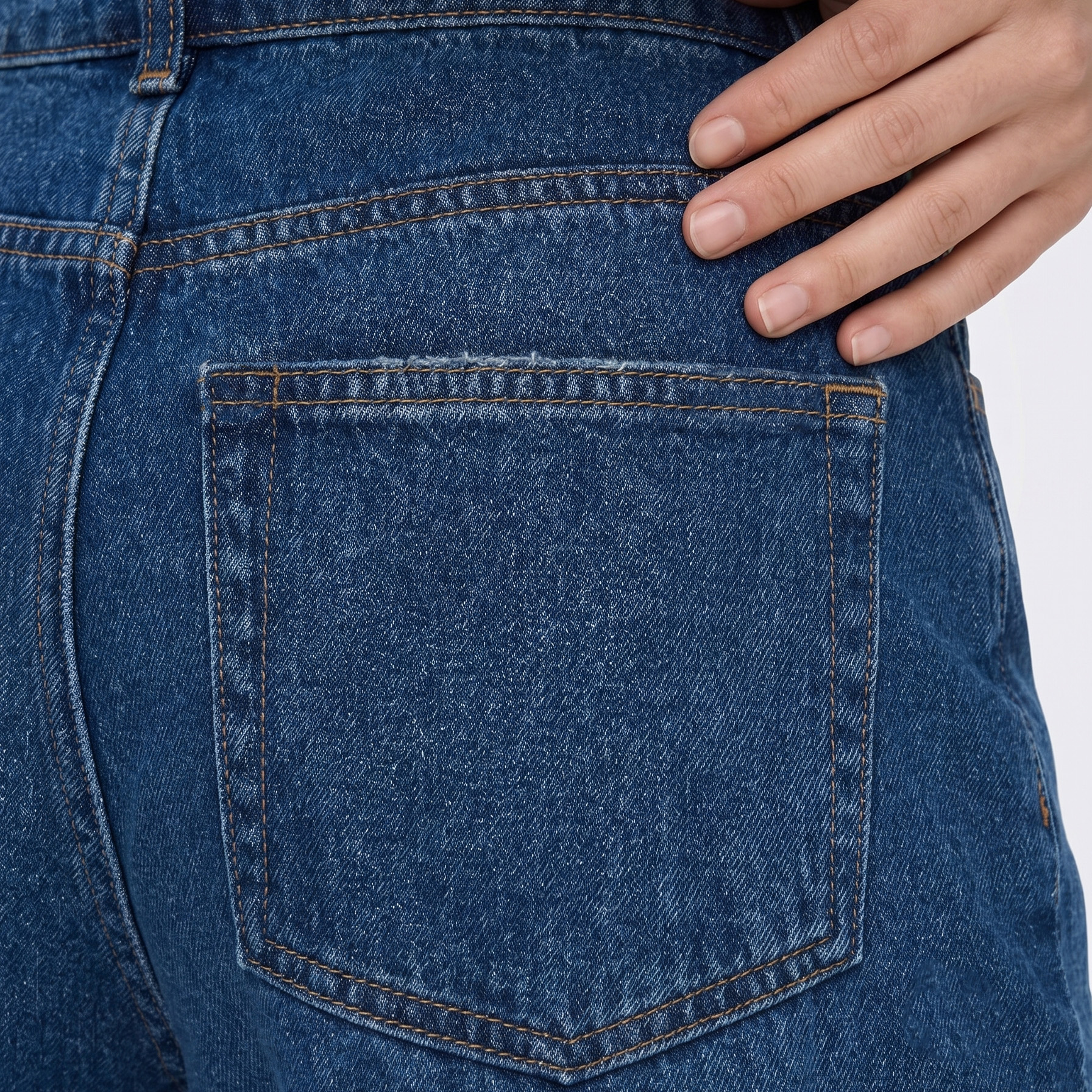 Jeans azuis em tecido denim com costuras castanhas e bolso traseiro com mão ao lado