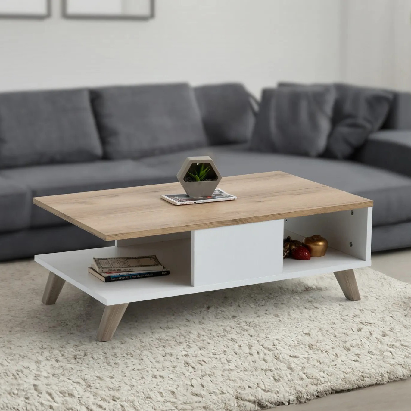 Mesa de centro em madeira clara com vasos decorativos e livros, com sofá cinza ao fundo