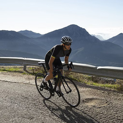 Ciclista com capacete e bicicleta preta numa estrada em zona montanhosa