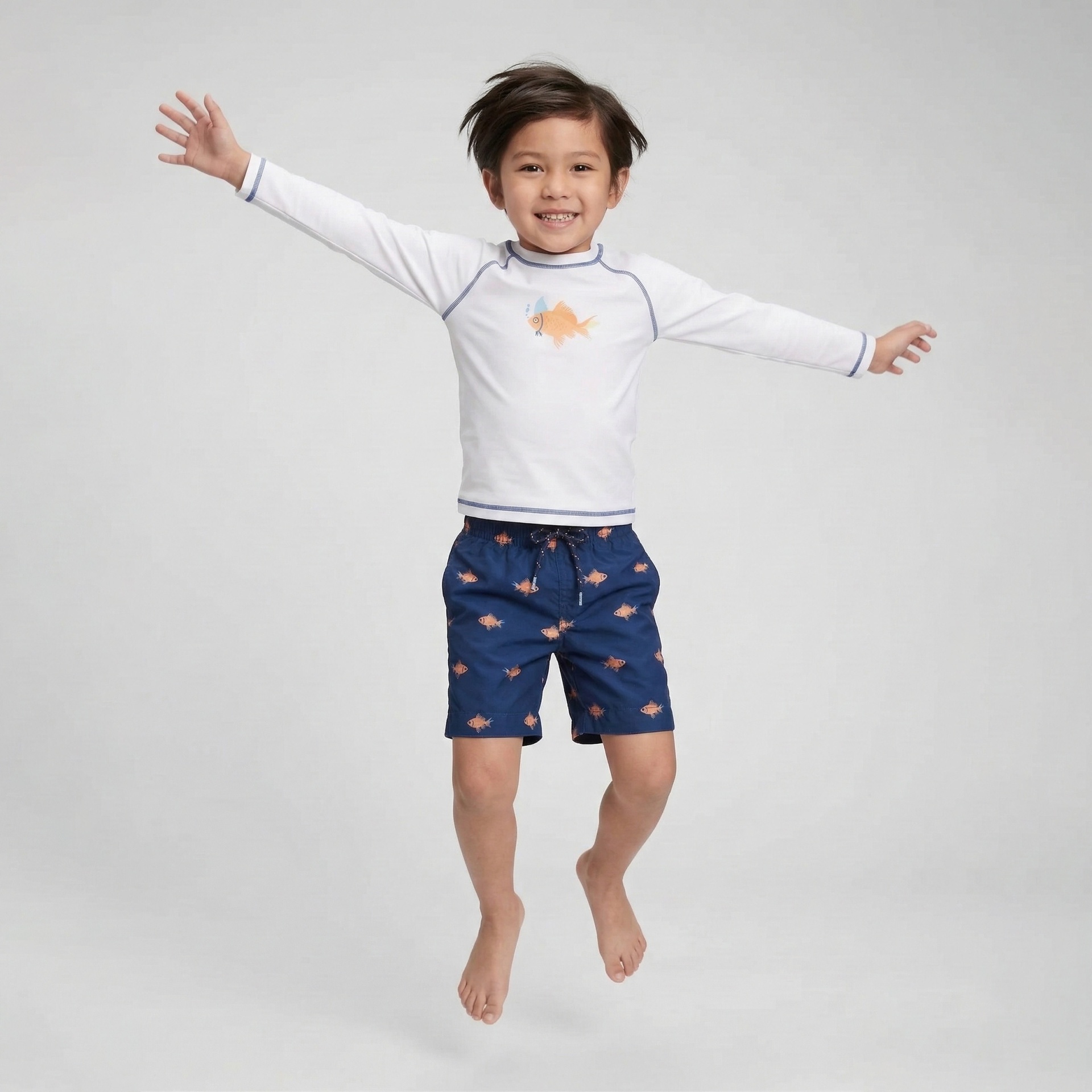 Criança a saltar com camisa branca de manga comprida com estampa de peixe laranja e calções azuis estampados com peixes laranja