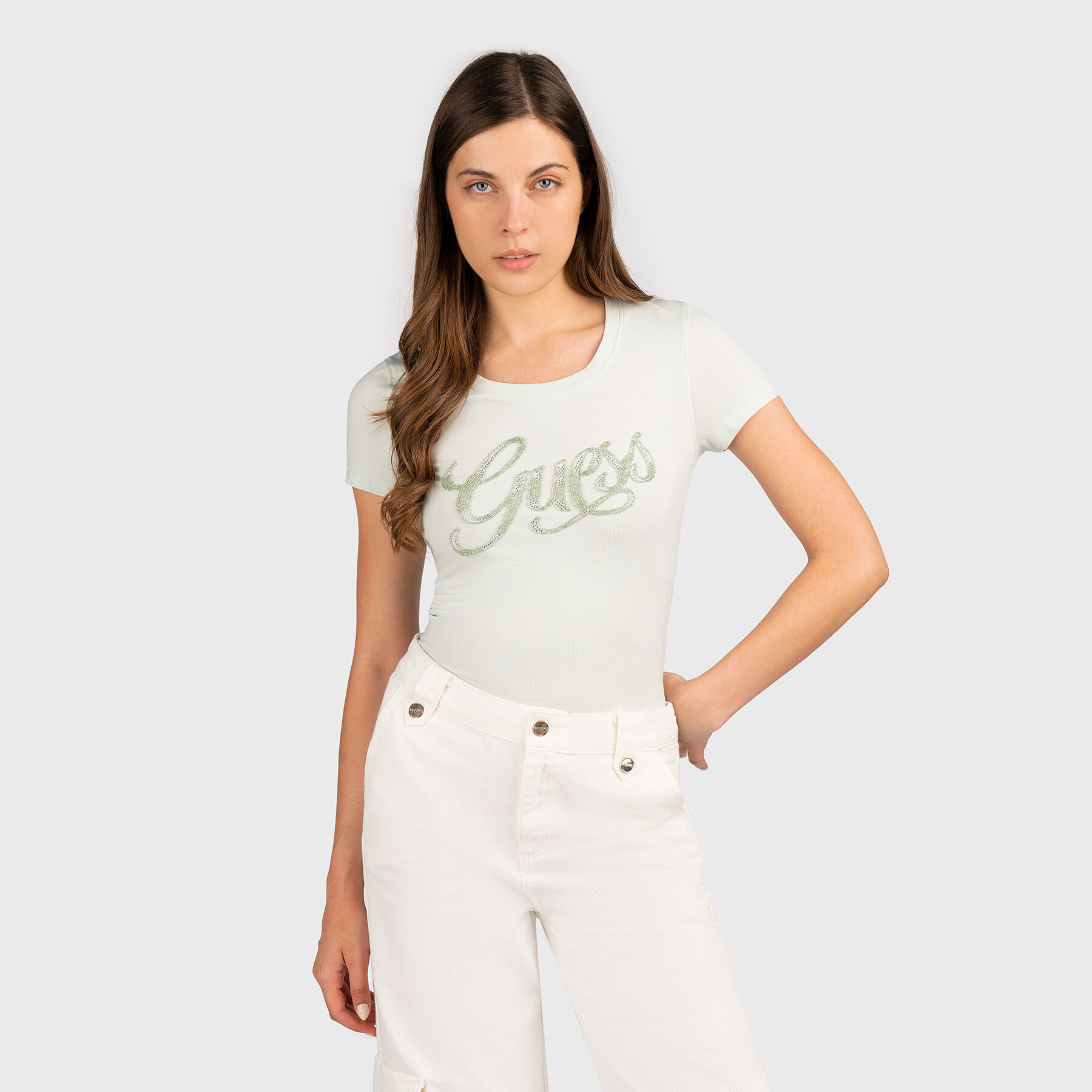 T-shirt branca de manga curta com logo Guess em letras verdes e calças brancas.