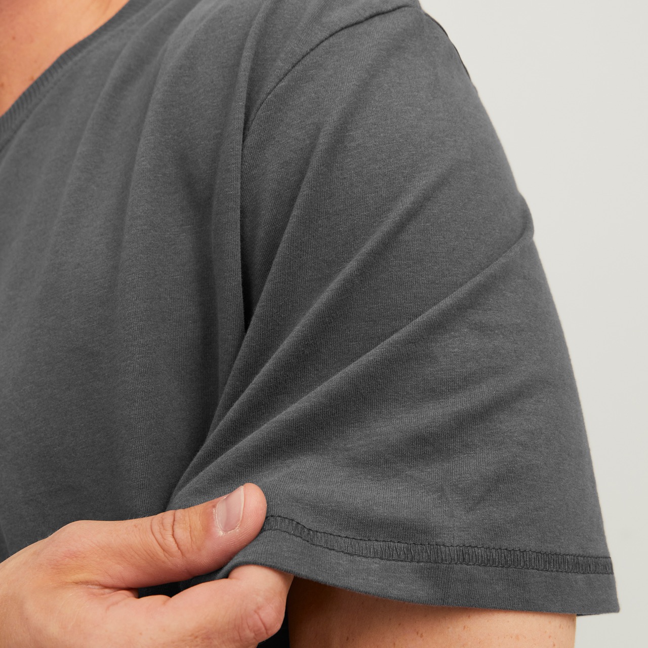 Manga e peito de t-shirt cinza escura com costura visível, sendo segurada por mão.