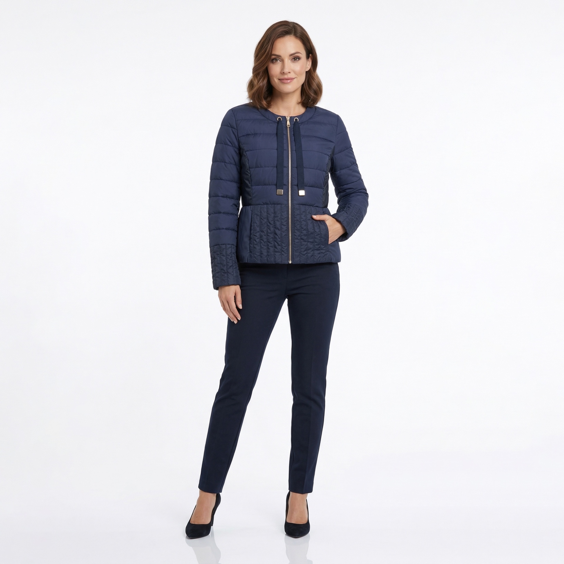 Mulher com casaco acolchoado azul escuro, calças justas azuis escuras e saltos negros num fundo branco.