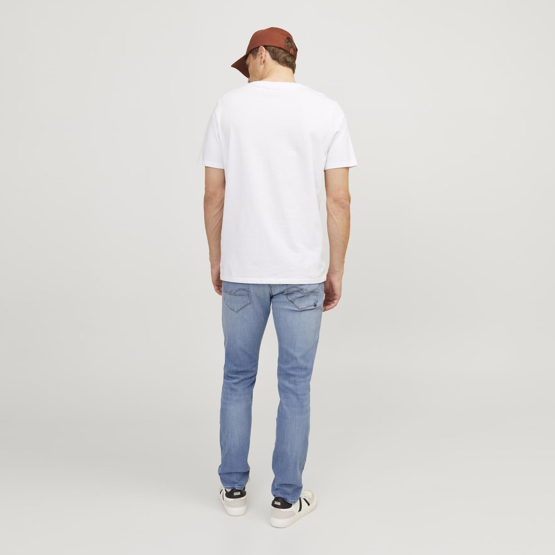 Homem com t-shirt branca, calças de ganga azuis claras e ténis brancos visto de costas