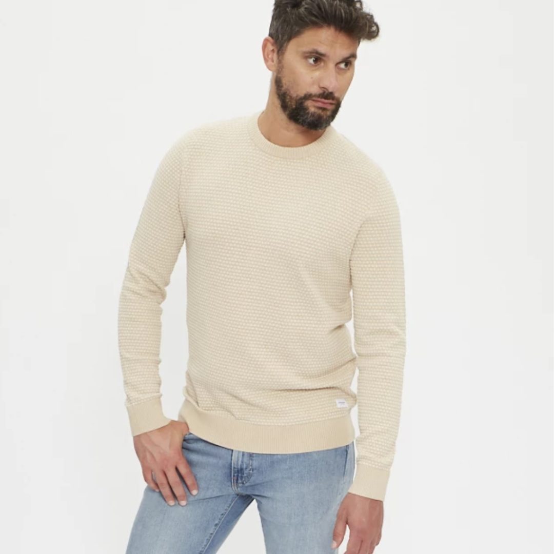 Homem com camisola bege texturada e jeans azuis claros