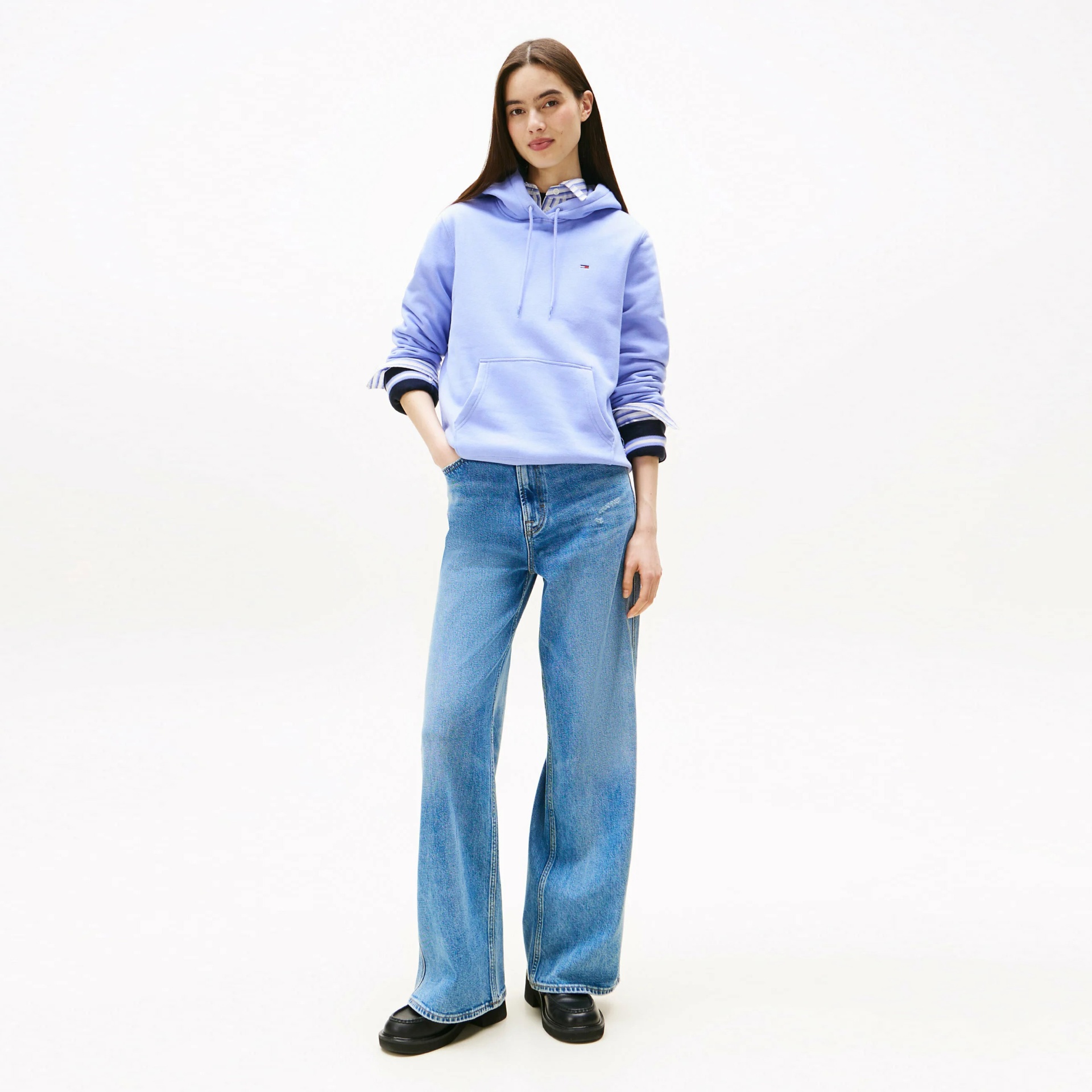 Mulher vestindo hoodie azul claro, camisa riscada e calças de ganga largas