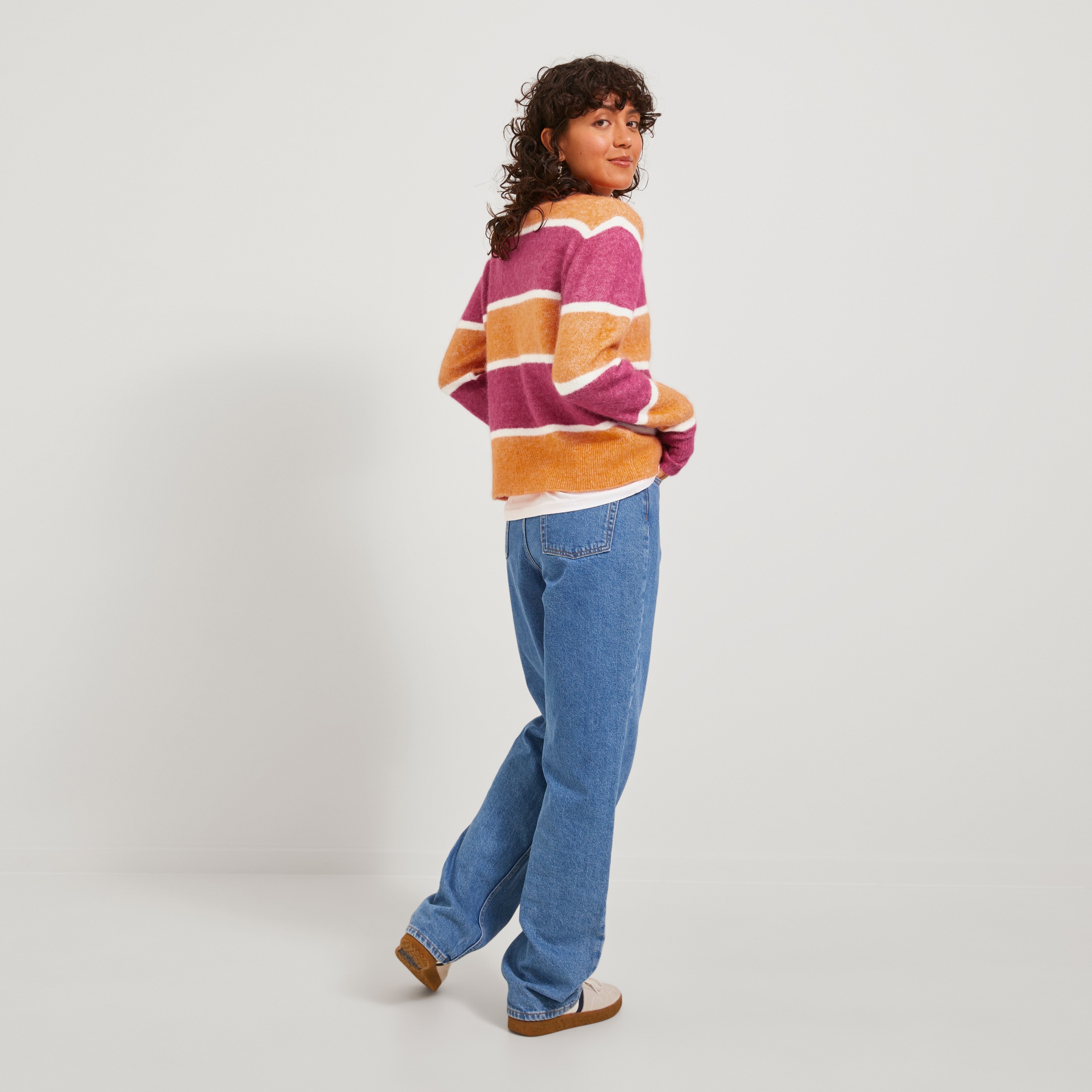 Mulher com sweater riscas e calças de ganga azuis, fundo branco